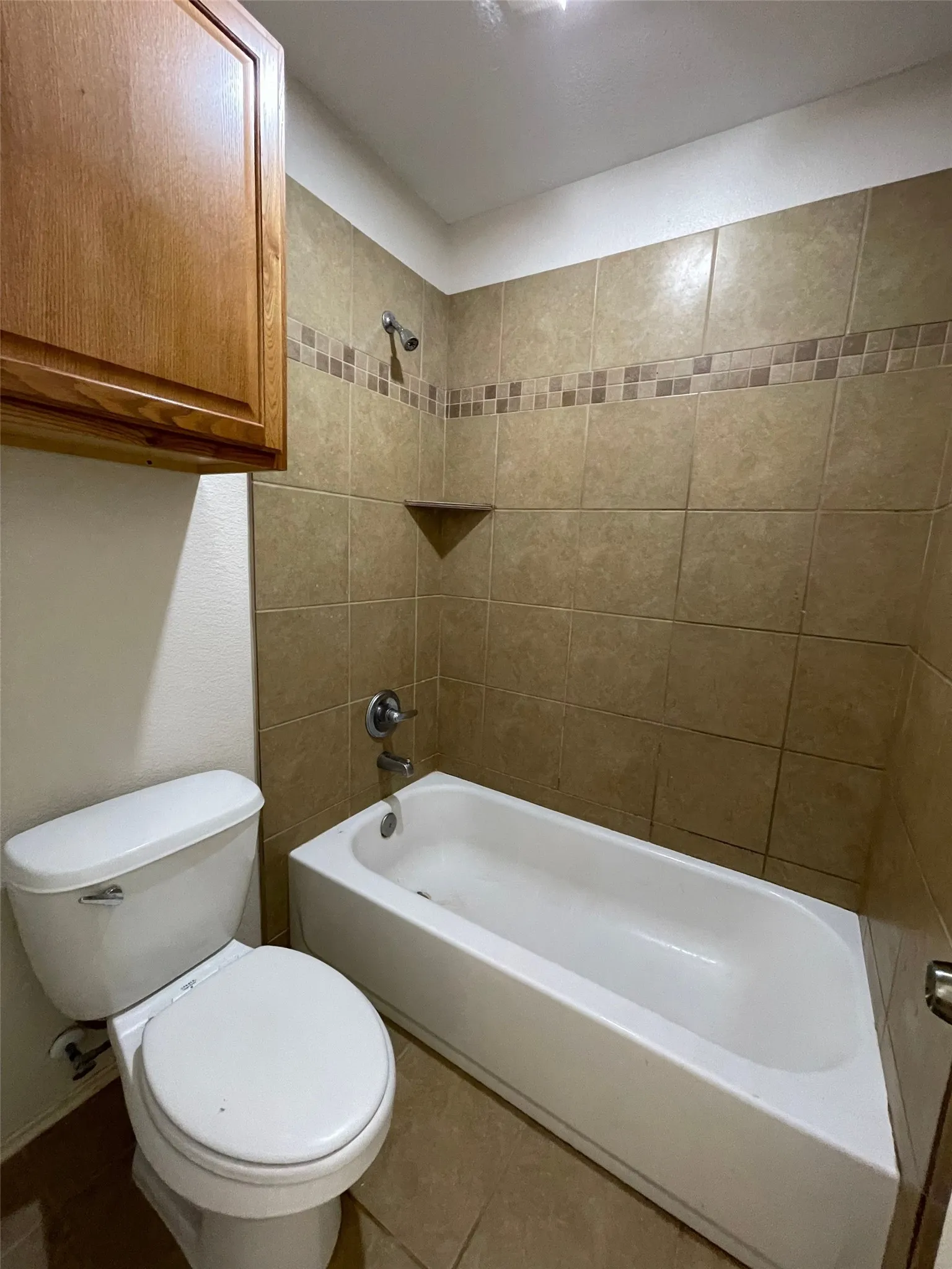 Tub/shower combination featuring tile surround with decorative accent band and built-in corner shelf