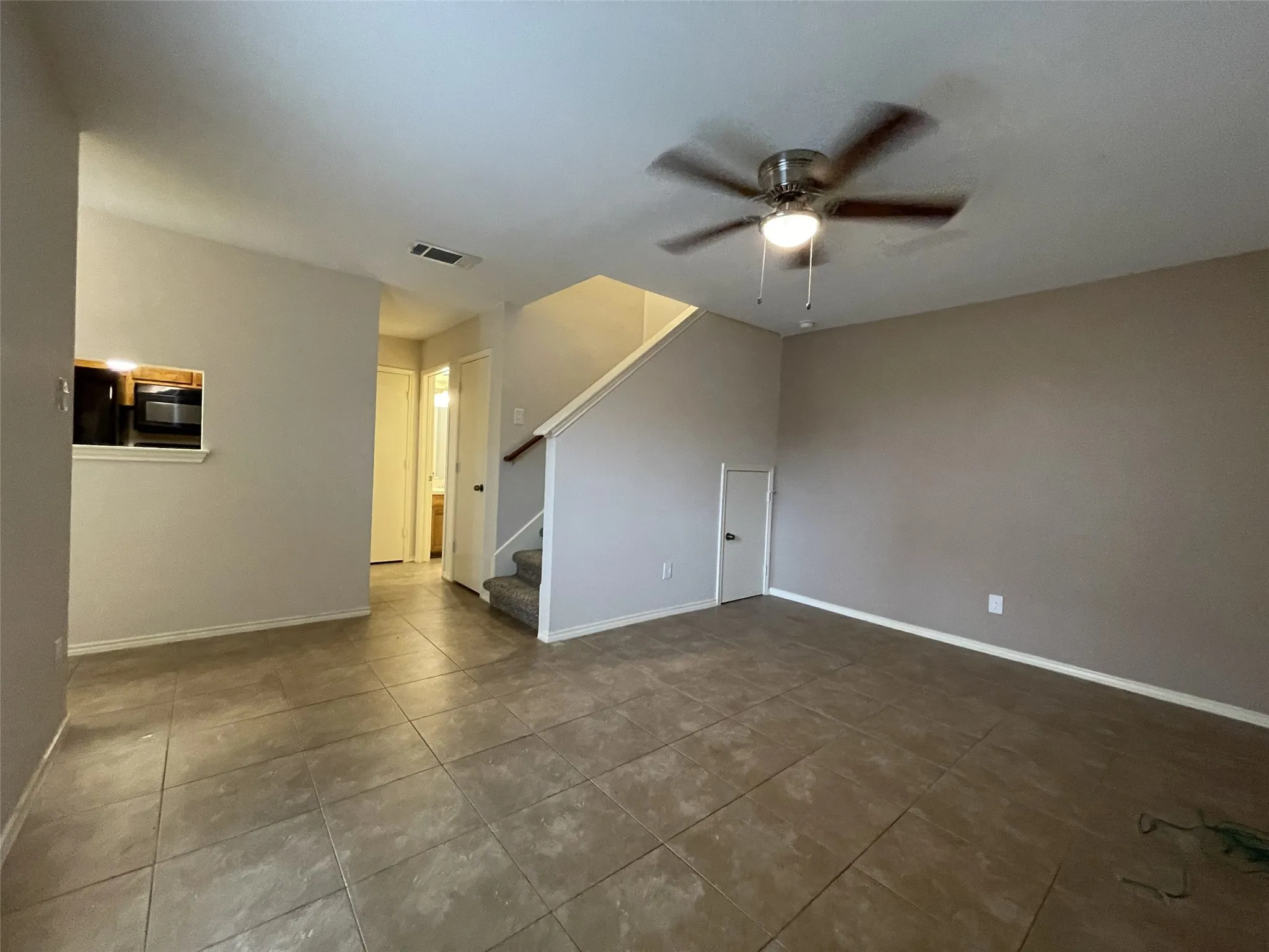 Tile flooring, ceiling fan with integrated lighting, built-in microwave, wood handrail, and carpeted stairs