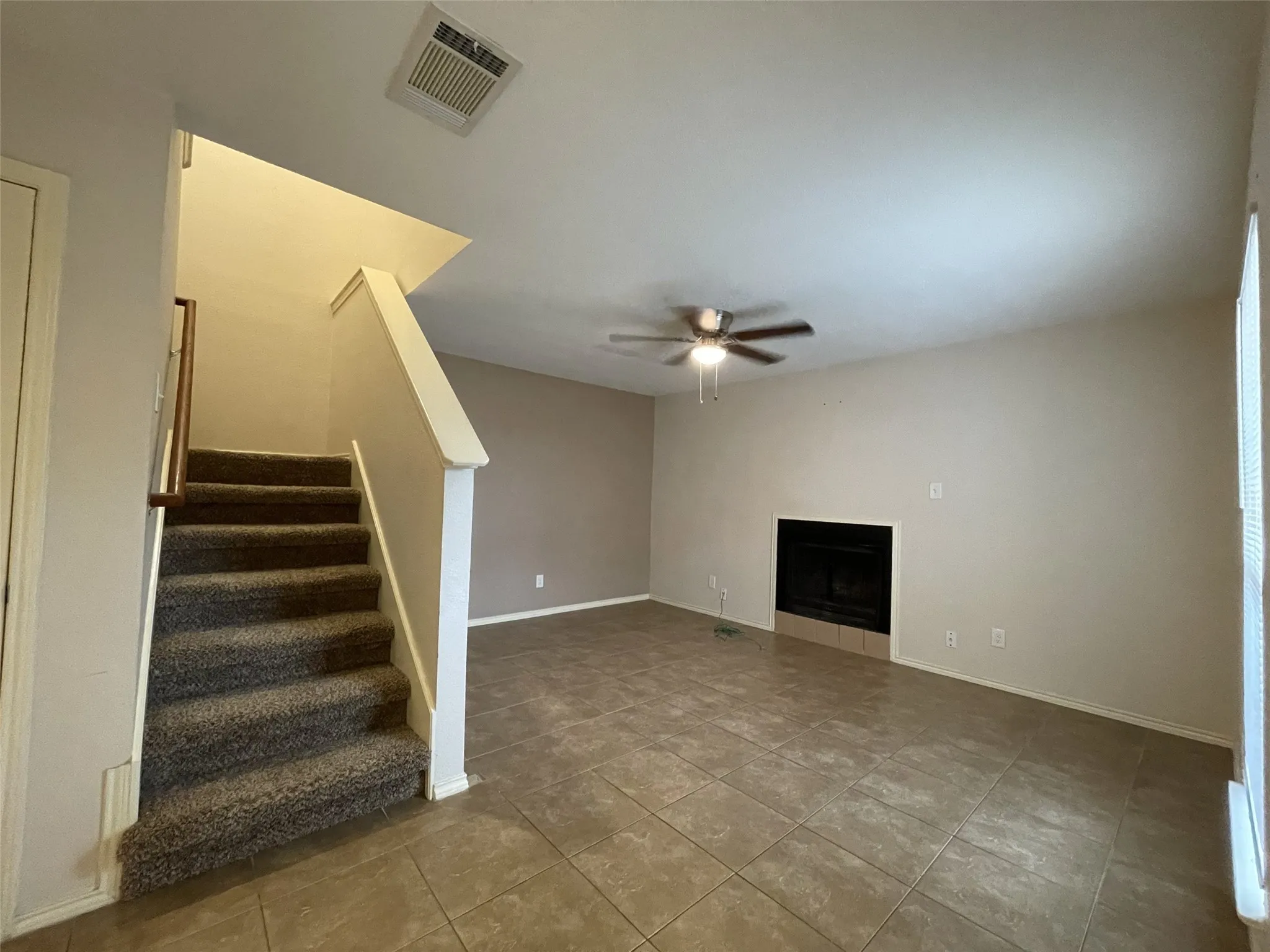 Living area featuring ceramic tile flooring, a fireplace with a tile hearth, a ceiling fan, and carpeted stairs leading to an upper level