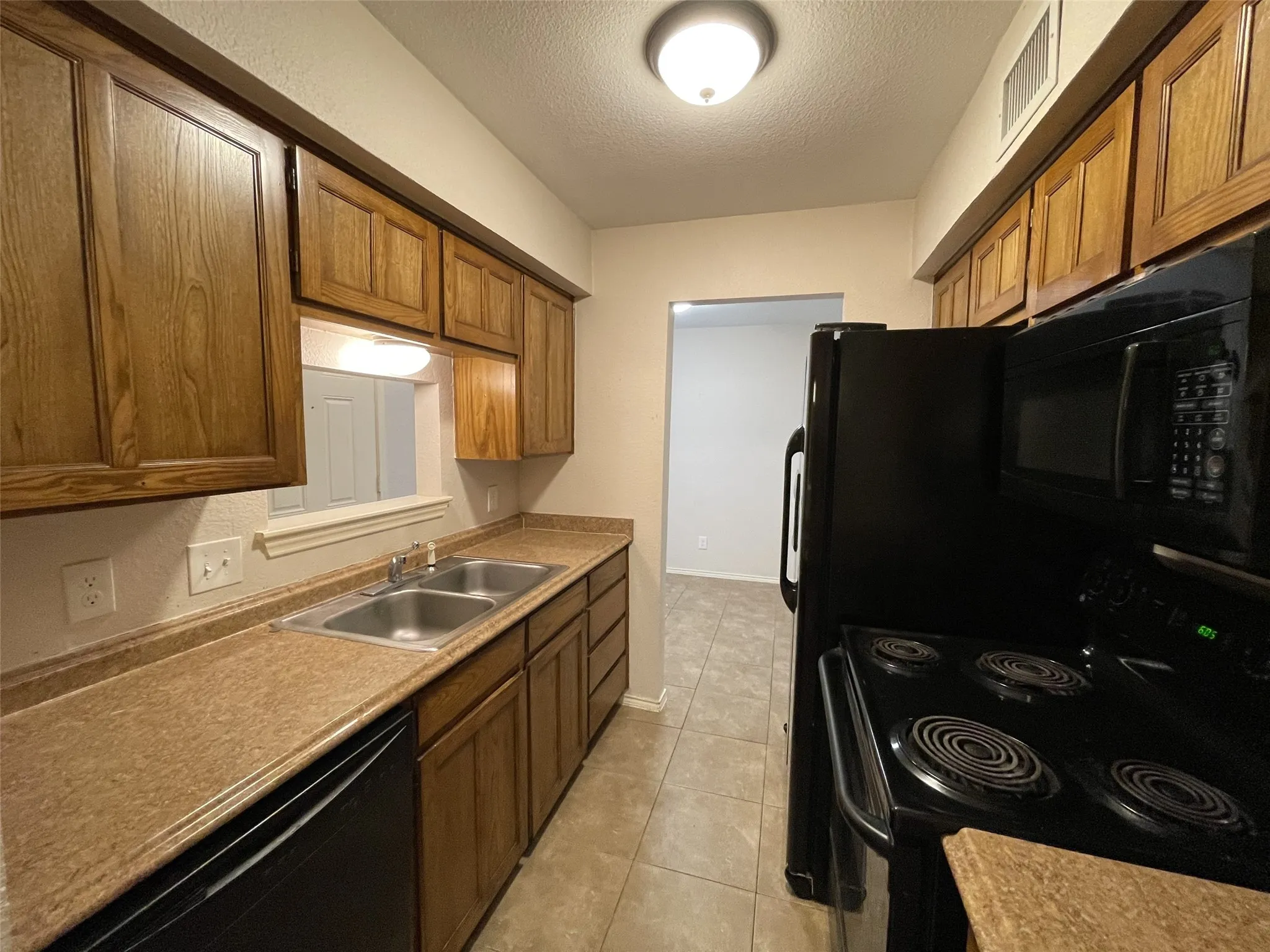 Kitchen featuring wood-finish cabinetry, a double basin stainless steel sink, black appliances, and tile flooring