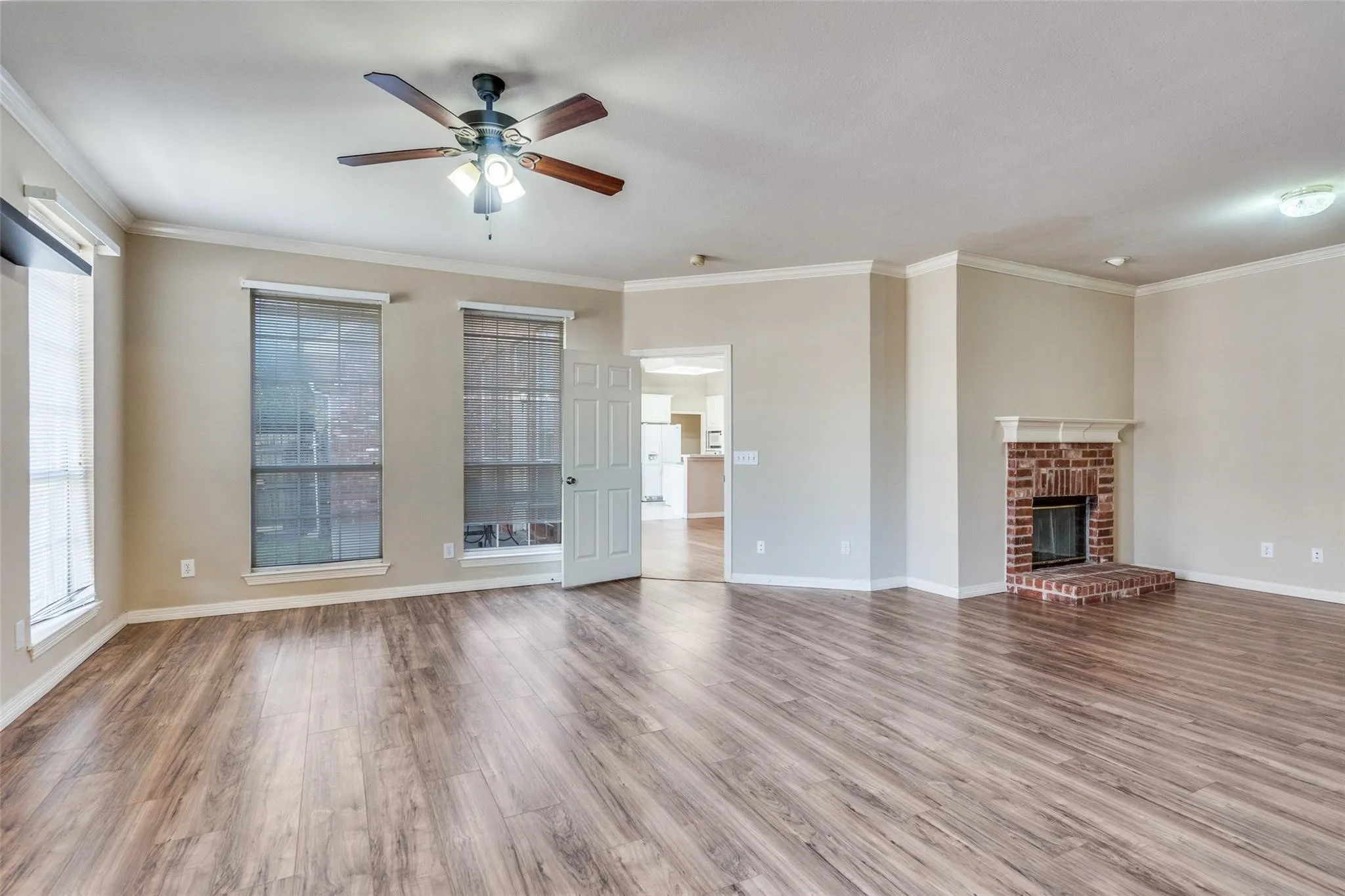 Spacious room featuring wood-finish flooring, a brick fireplace with a white mantel, and multiple windows