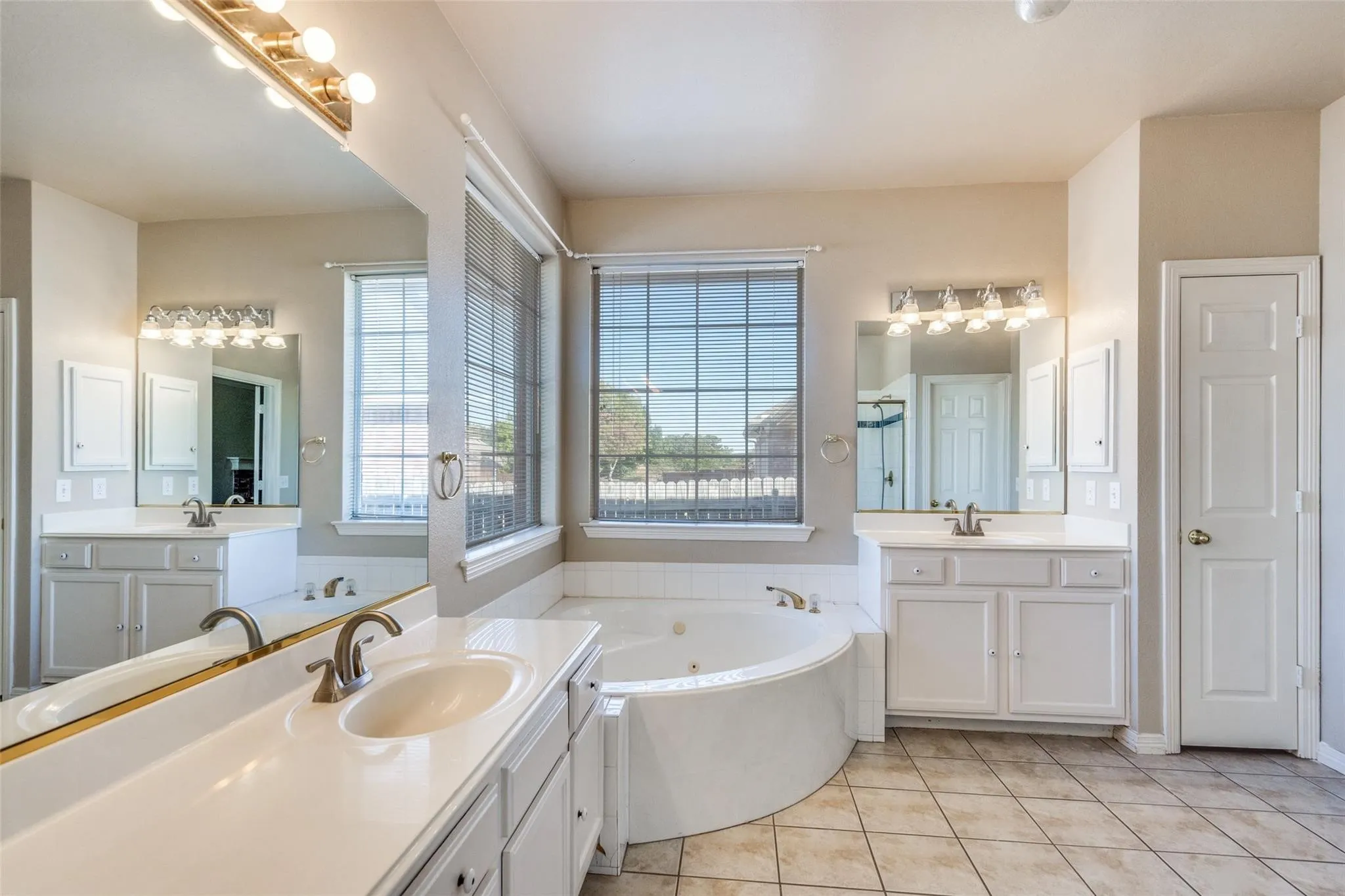 Dual vanity with integrated sinks, a corner soaking tub, two large windows, and tiled flooring