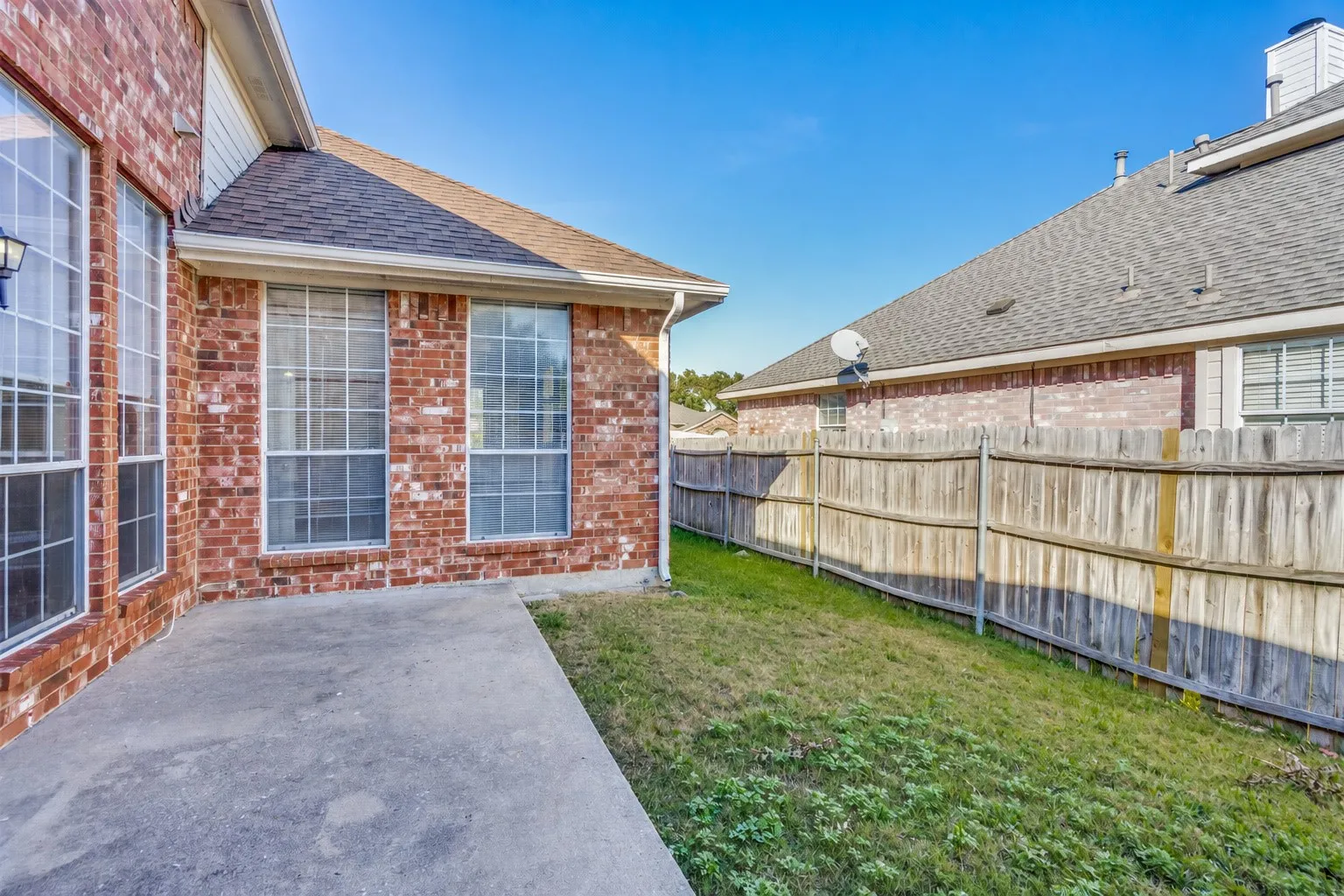 Brick exterior with multiple windows, concrete patio, and sloped grass area
