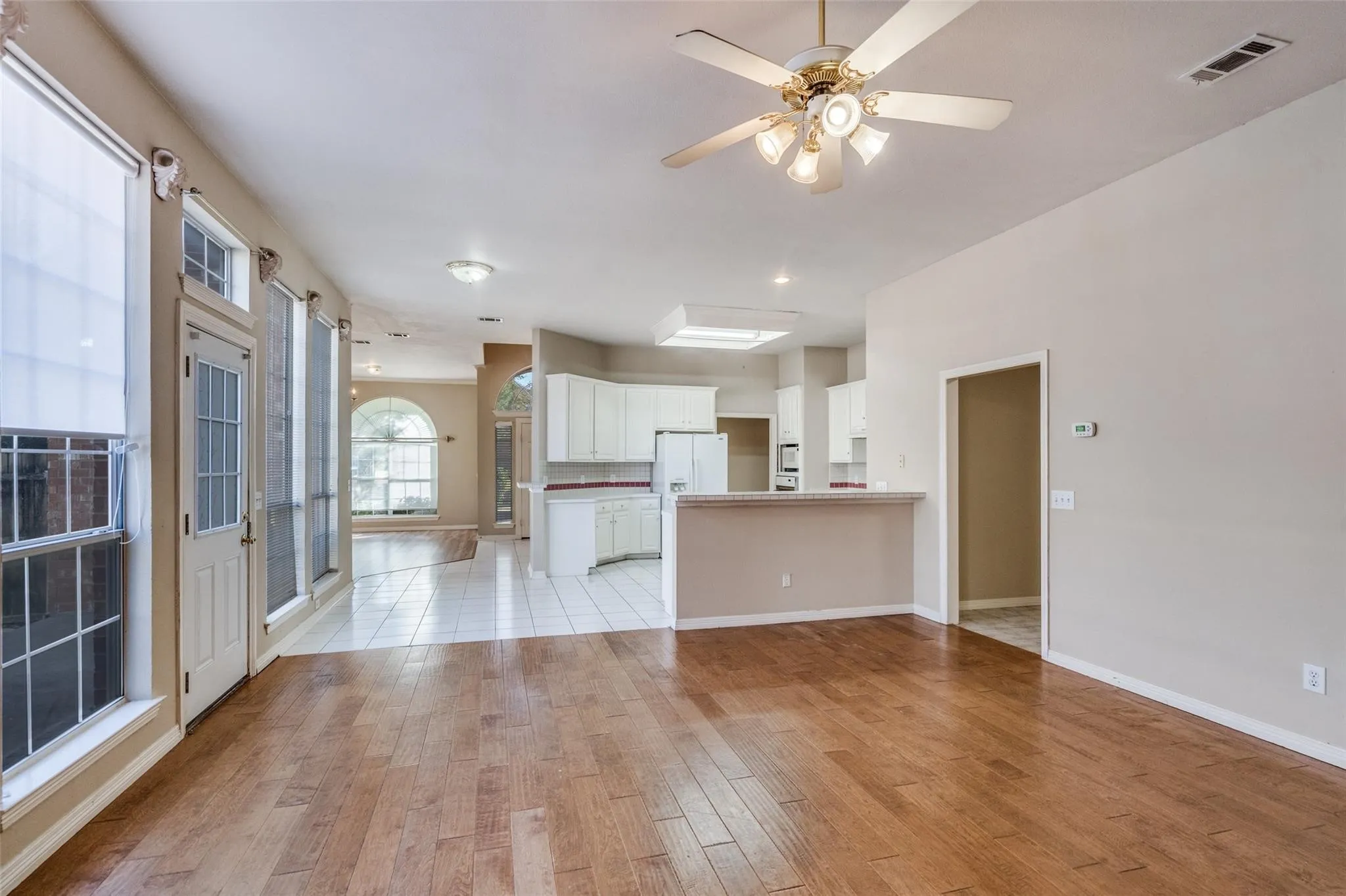 Hardwood-style flooring throughout, white tiled flooring, arched window, ceiling fan with integrated lighting, and recessed lighting
