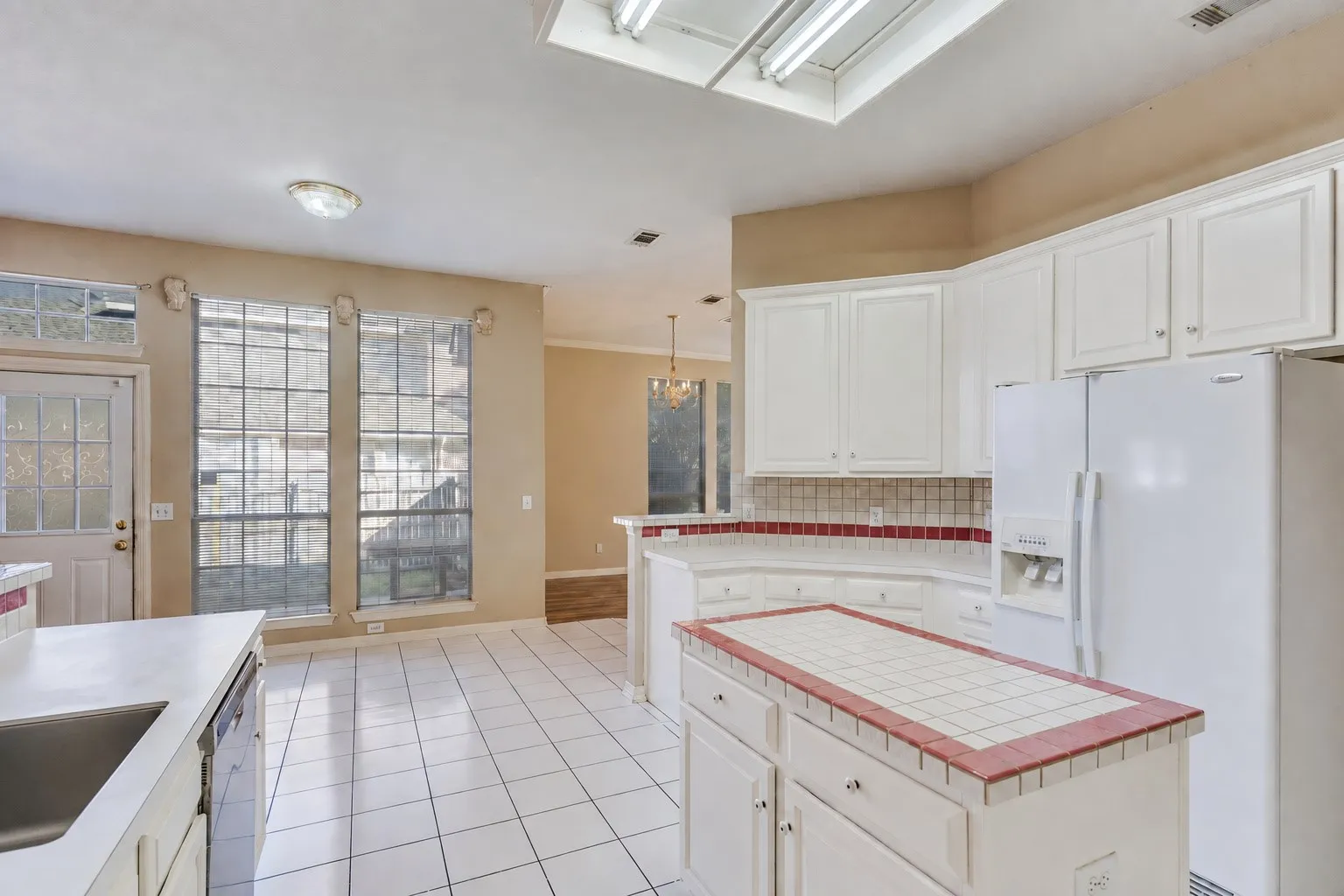 White cabinetry with a tiled backsplash, center island with tiled countertop, and white tile flooring