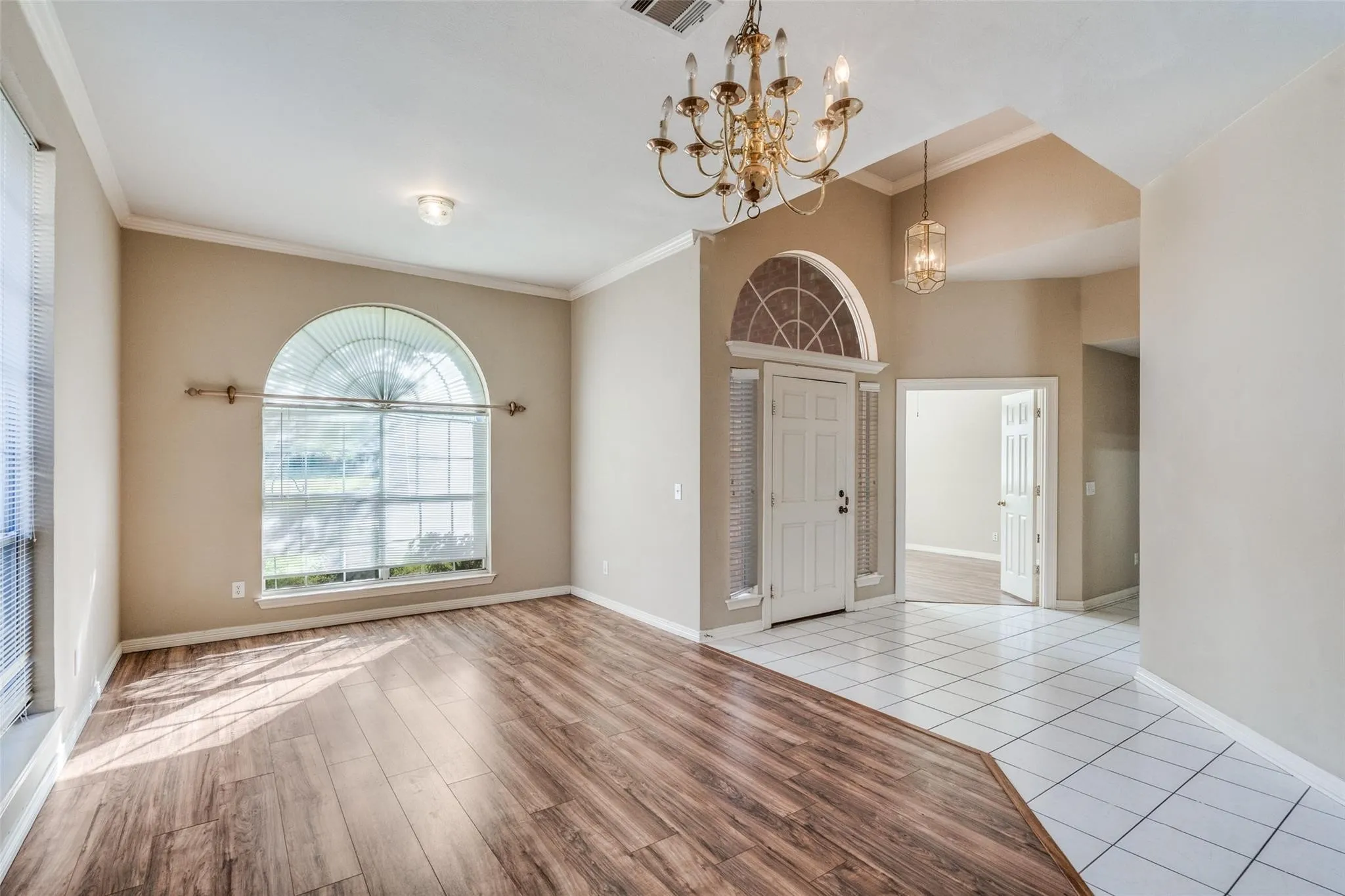 Arched window with decorative trim, wood-finish flooring, tiled entry, tray ceiling, and a traditional chandelier