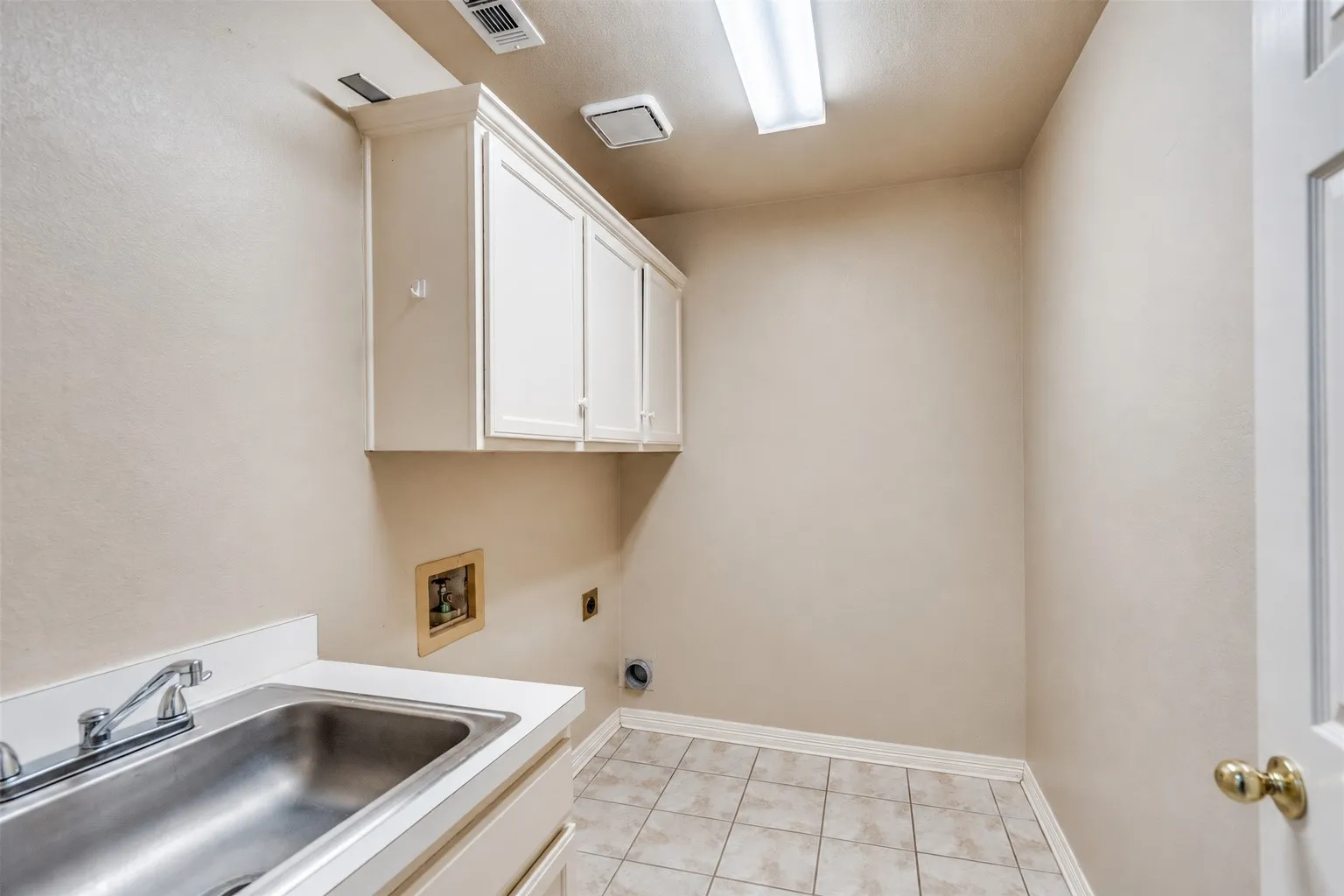 Utility room featuring a stainless steel basin sink, white cabinetry, and tile flooring