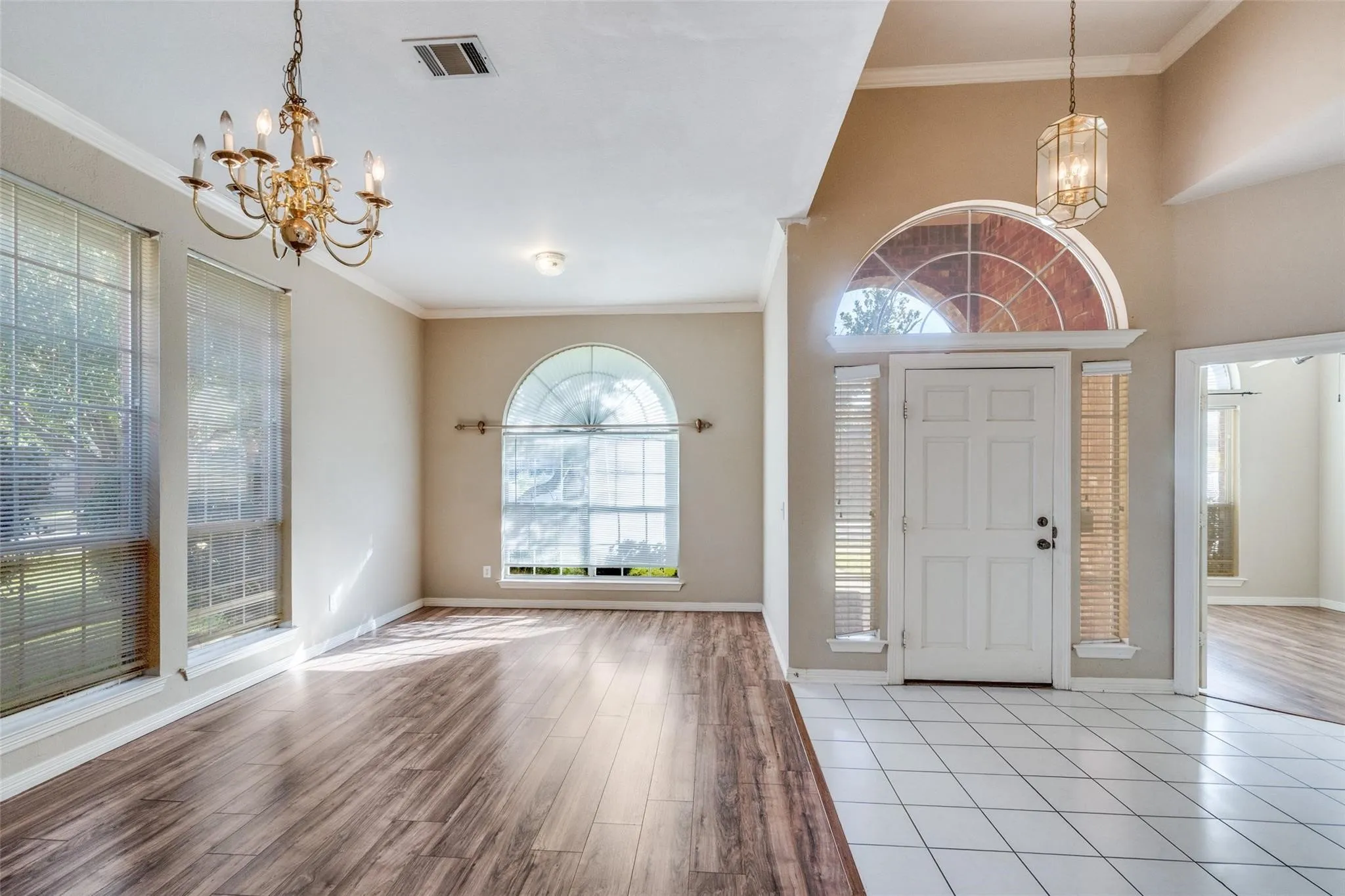 Vaulted entry with transom window and sidelights, wood-finish flooring, white tile flooring, and decorative chandeliers