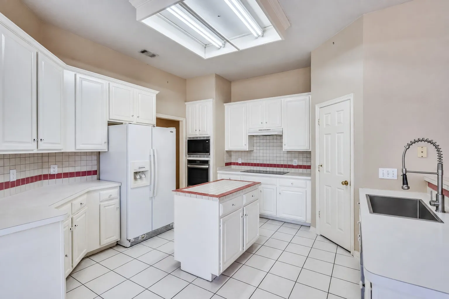Kitchen featuring white cabinetry, an integrated double oven, an island, a stainless steel sink, and tile flooring