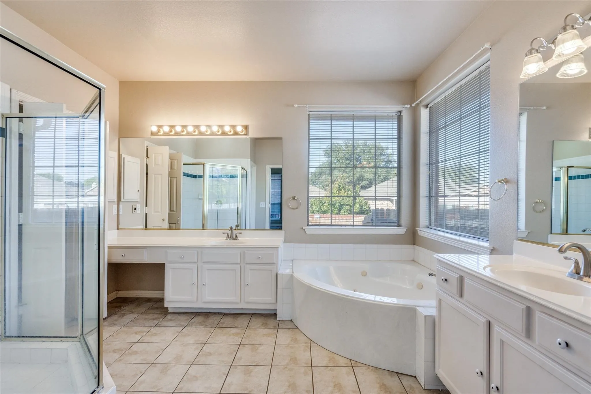 Shower enclosure with clear glass, corner jetted tub, dual vanities with white cabinetry, large mirror, and tiled flooring