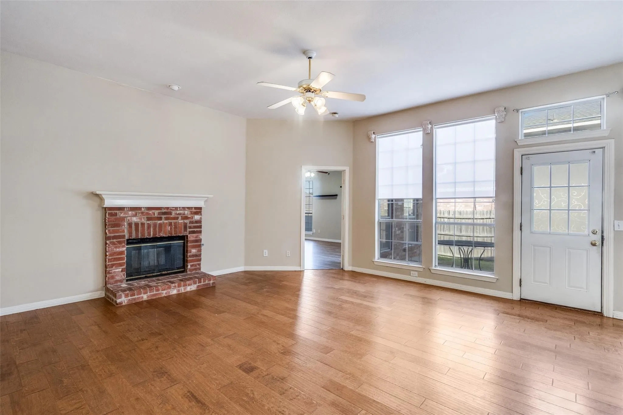 Brick fireplace with a white mantel, wood-finish flooring, and multiple windows