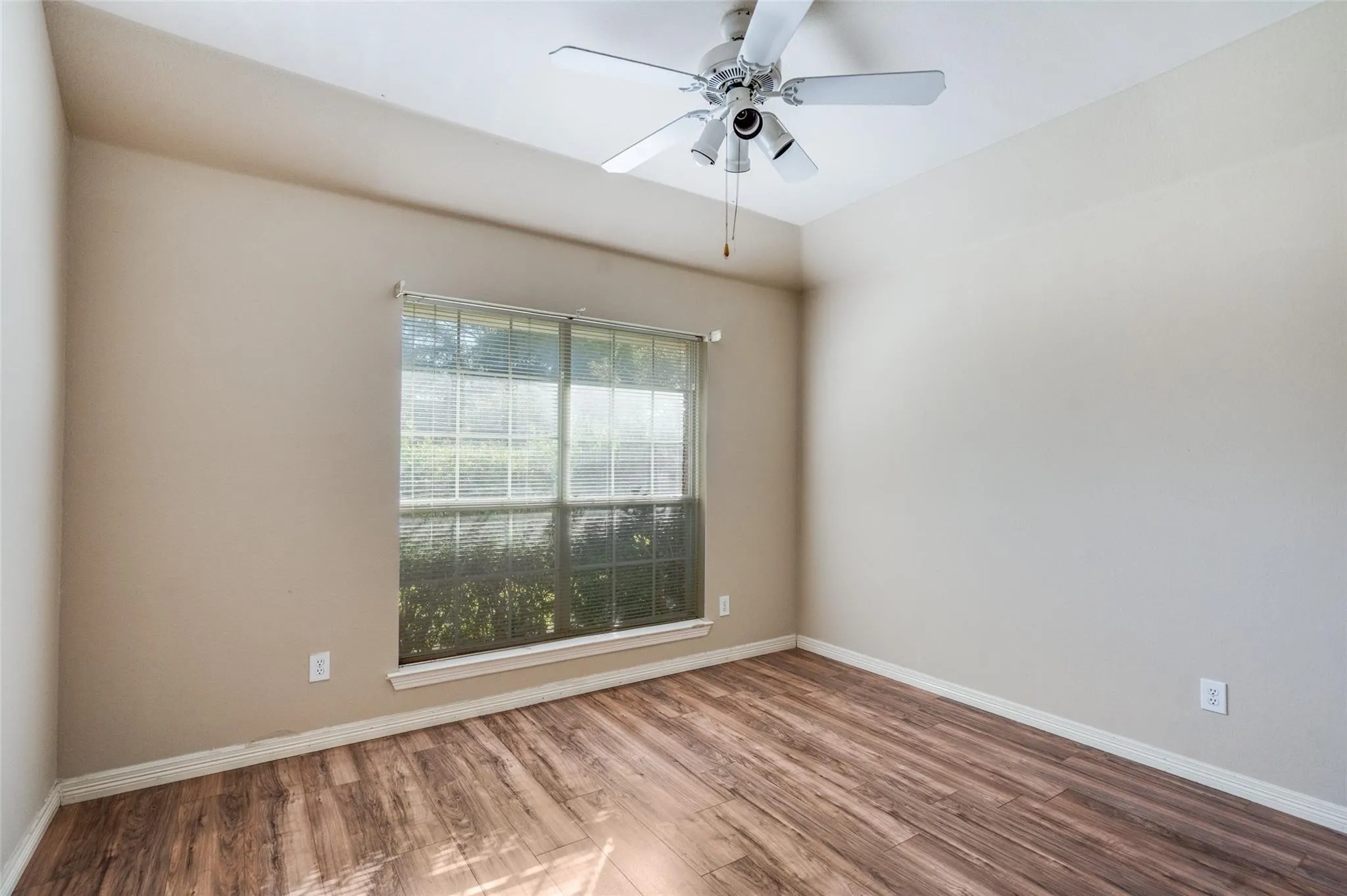 Vaulted ceiling with a ceiling fan light fixture, wood-finish flooring, and a large window with blinds