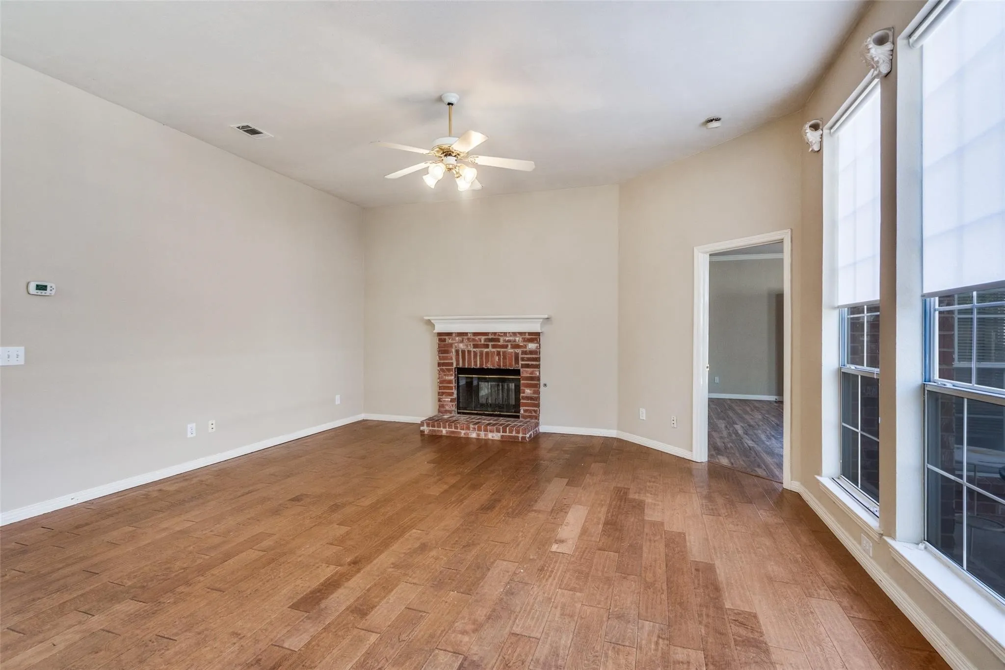 Wood-finish flooring throughout, vaulted ceiling, and a brick fireplace with a white mantel