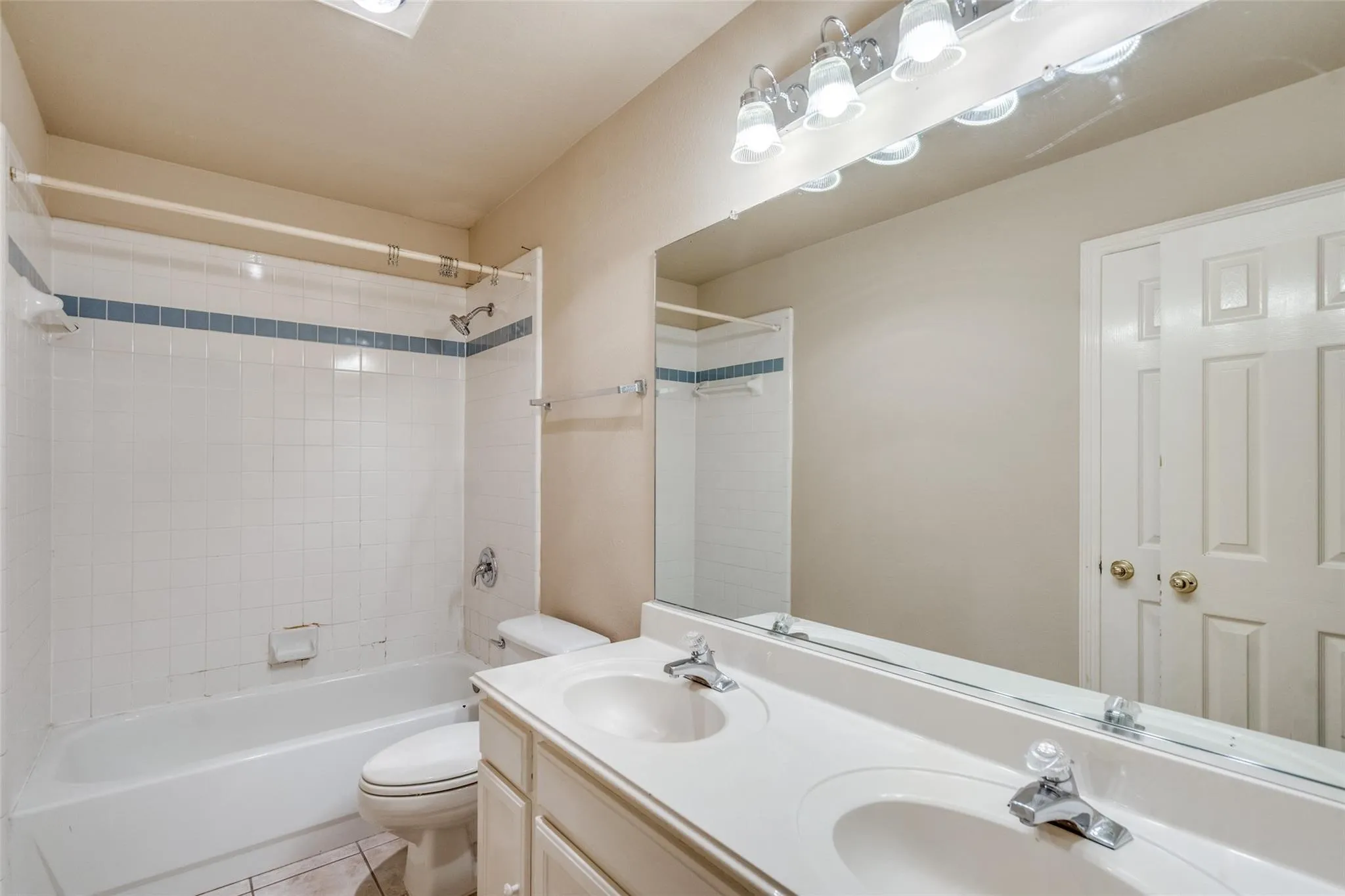 Dual vanity with integrated sinks, full-width mirror, white paneled doors, and a tiled tub/shower combination