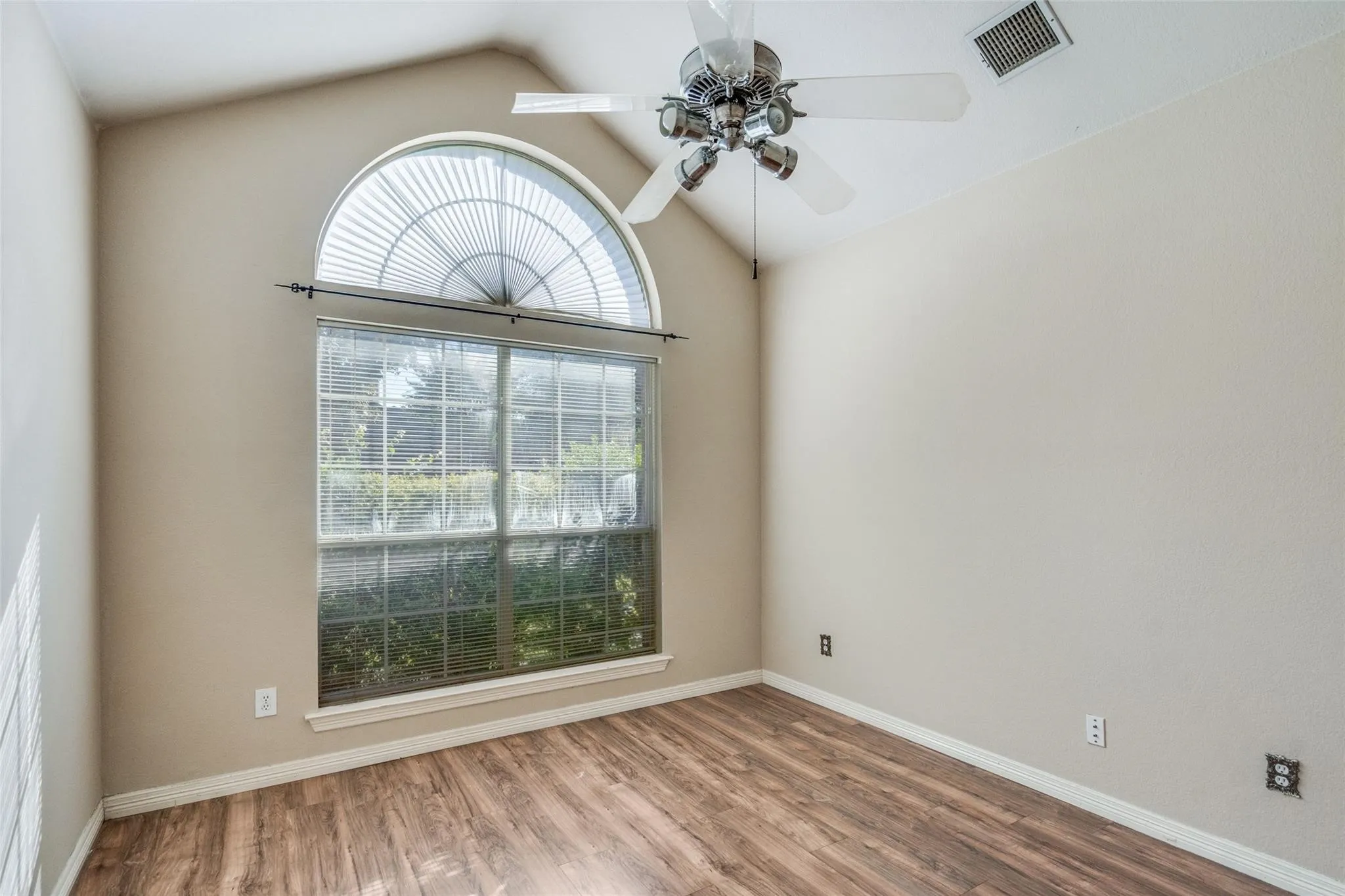 Vaulted ceiling, arched transom window, large rectangular window, wood-finish flooring, and ceiling fan