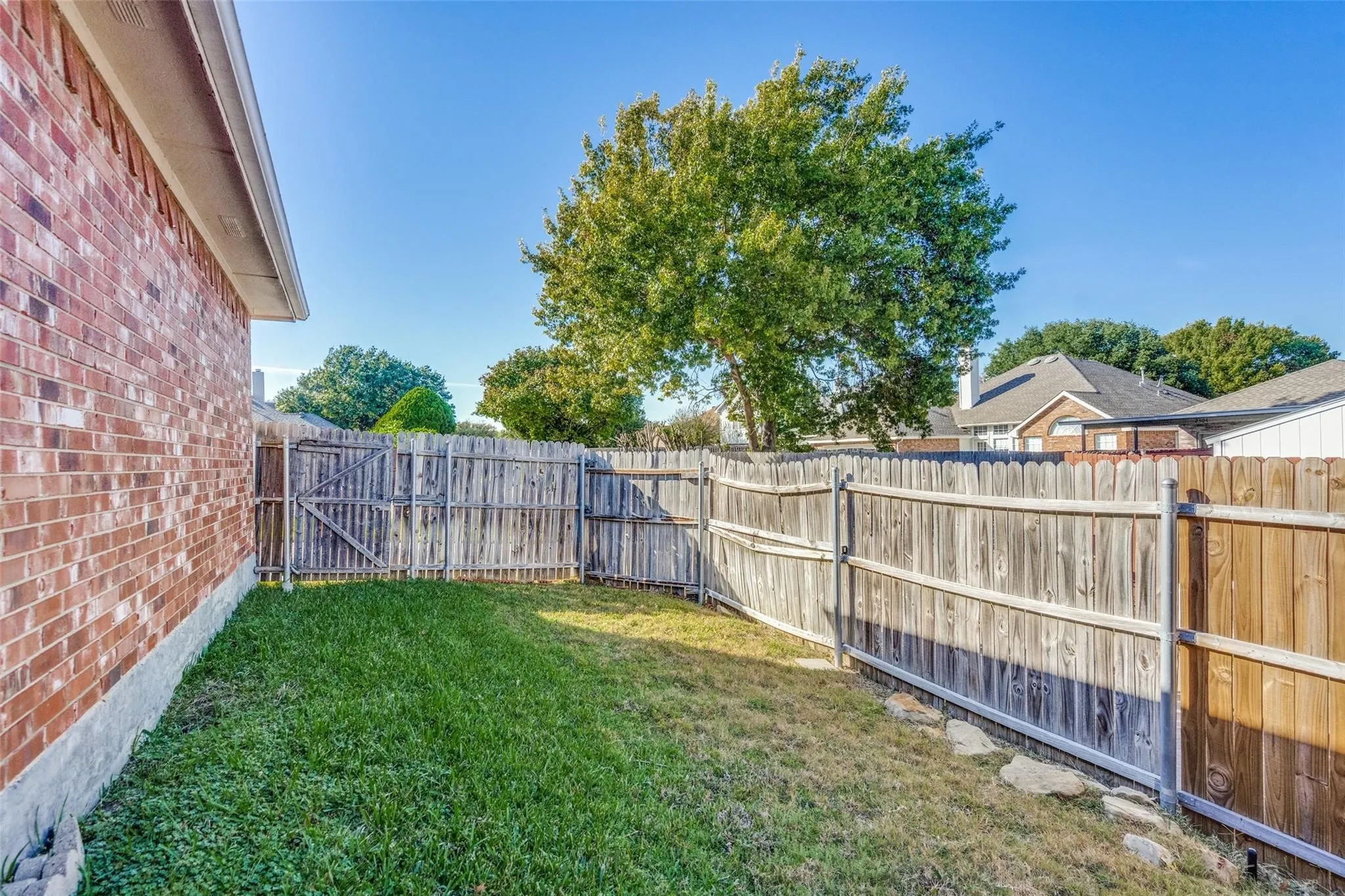 Enclosed backyard featuring a wood fence, a single gate, and a brick exterior