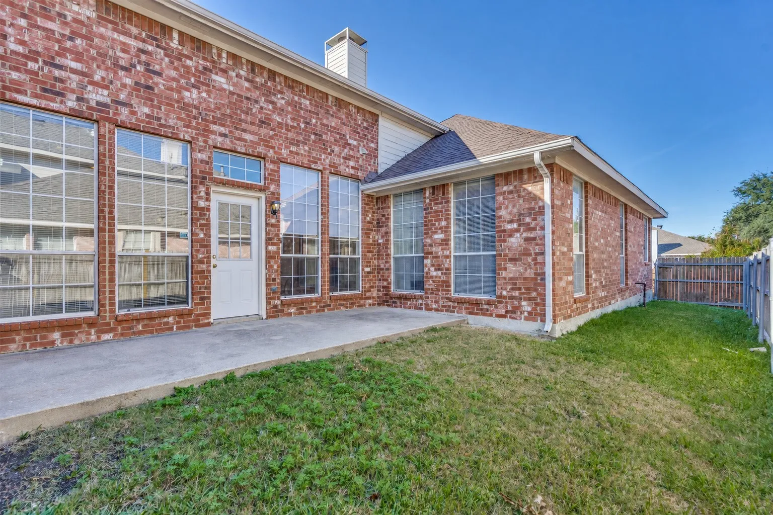 Brick exterior with multiple tall windows, concrete patio, white rear entry door, and a grass lawn