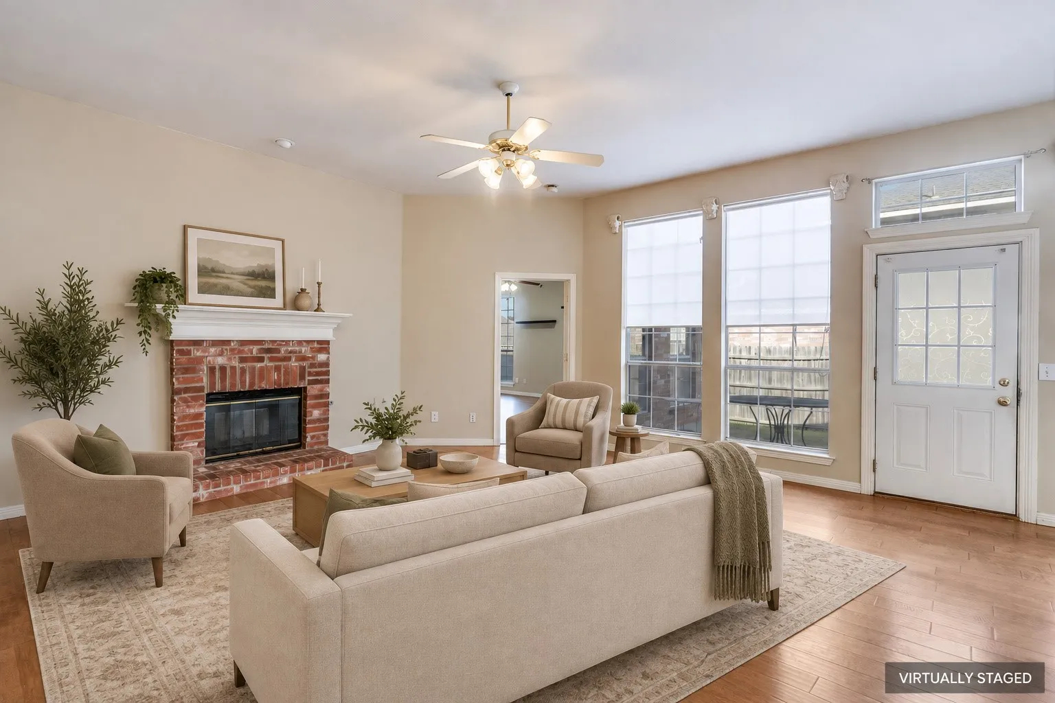Brick fireplace with a white mantel, wood-finish flooring, ceiling fan, and multiple windows for natural light