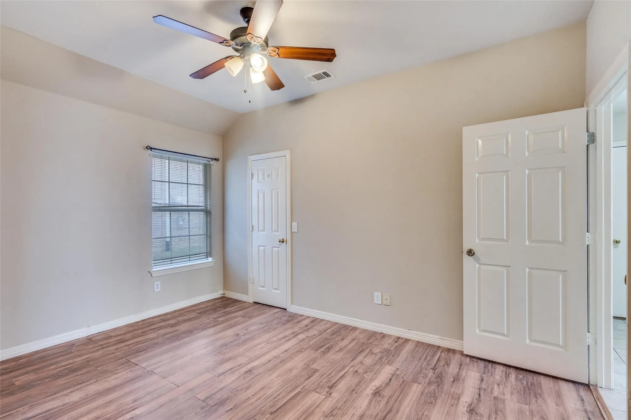 Vaulted ceiling with a ceiling fan, wood-finish flooring, and a paneled door