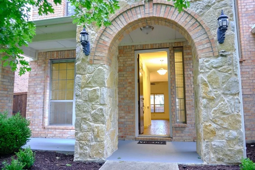 Brick and stone exterior featuring an arched entryway, decorative wall sconces, and a paneled entry door with sidelight