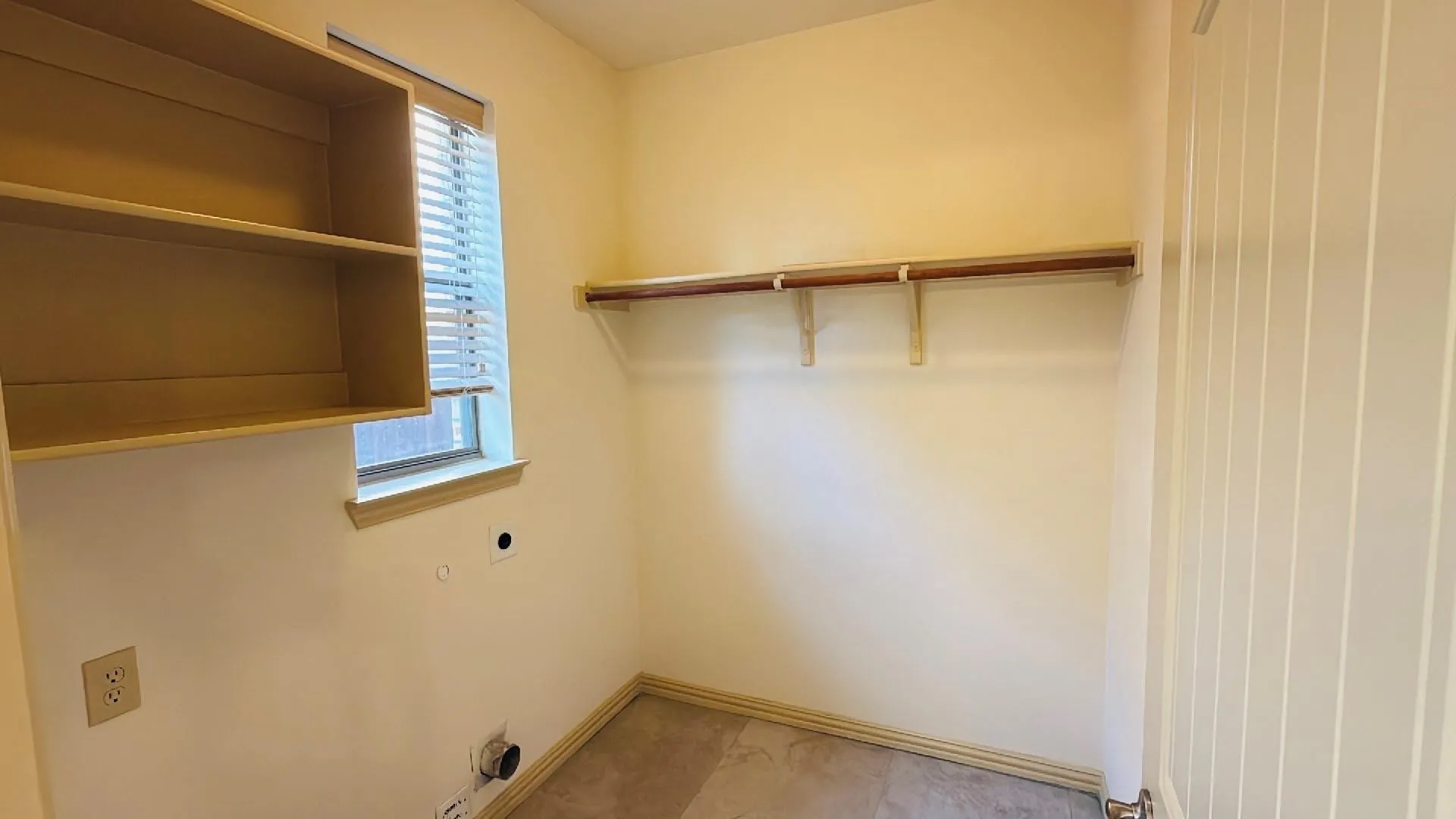 Laundry area featuring built-in shelving, a window with blinds, and a clothing rod