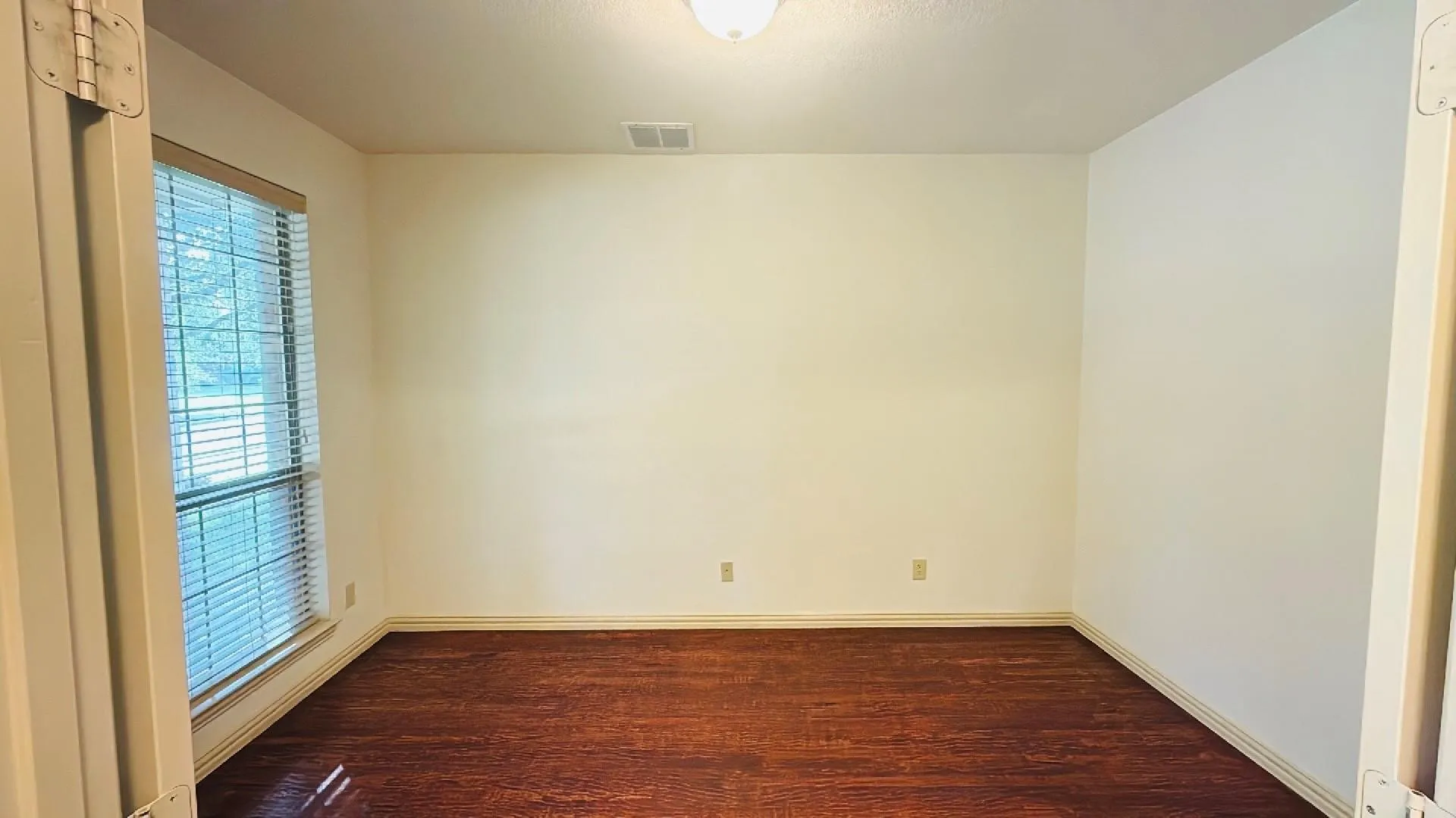 Wood-finish flooring with white baseboards, a window with horizontal blinds, and a ceiling-mounted light fixture