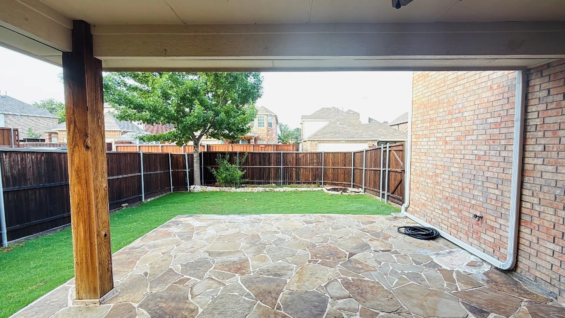 Covered patio featuring flagstone paving, brick exterior wall, and a wood support column