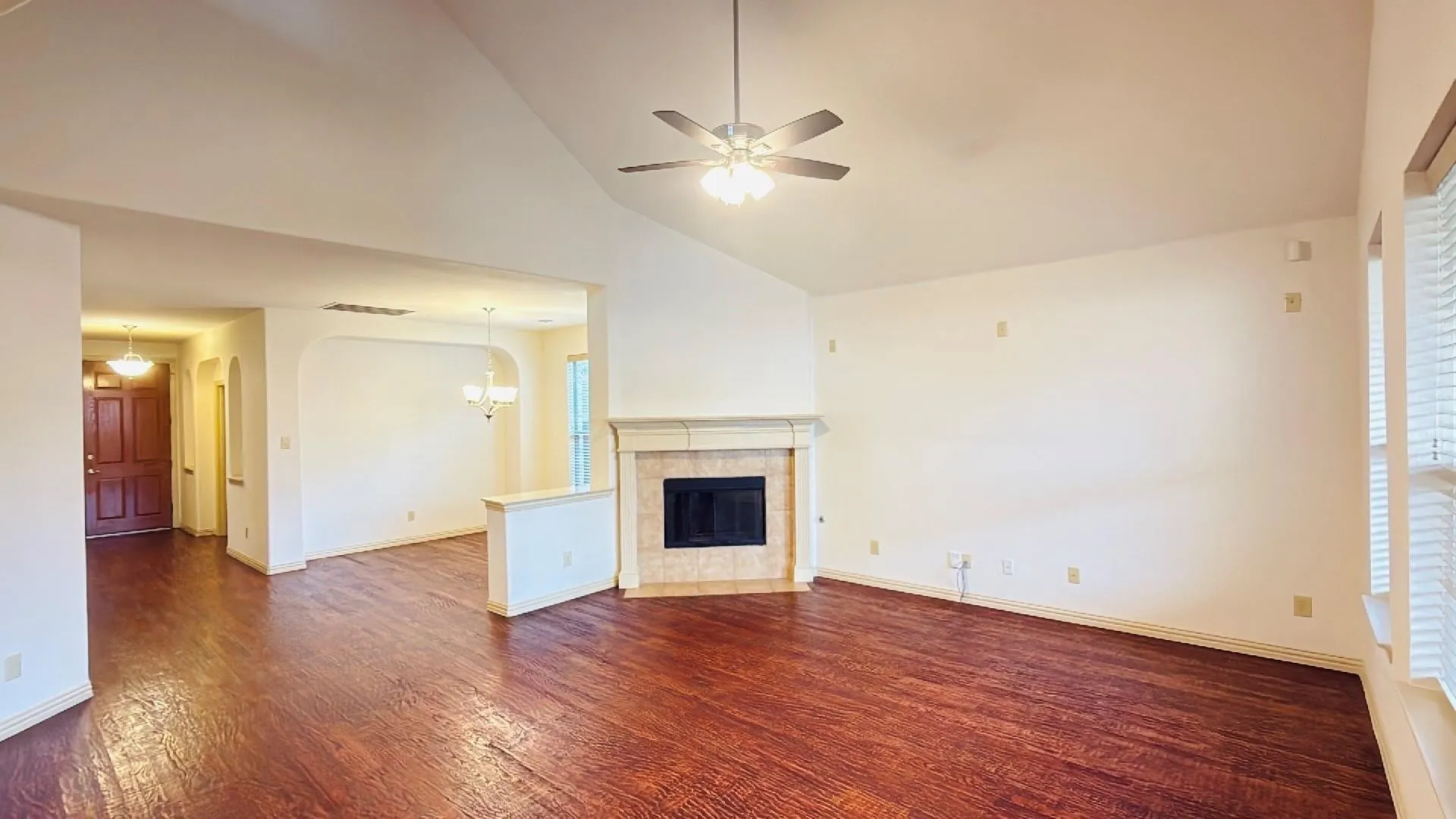 Vaulted ceiling with ceiling fan, wood-finish flooring, corner fireplace with stone surround and mantle, and arched doorways