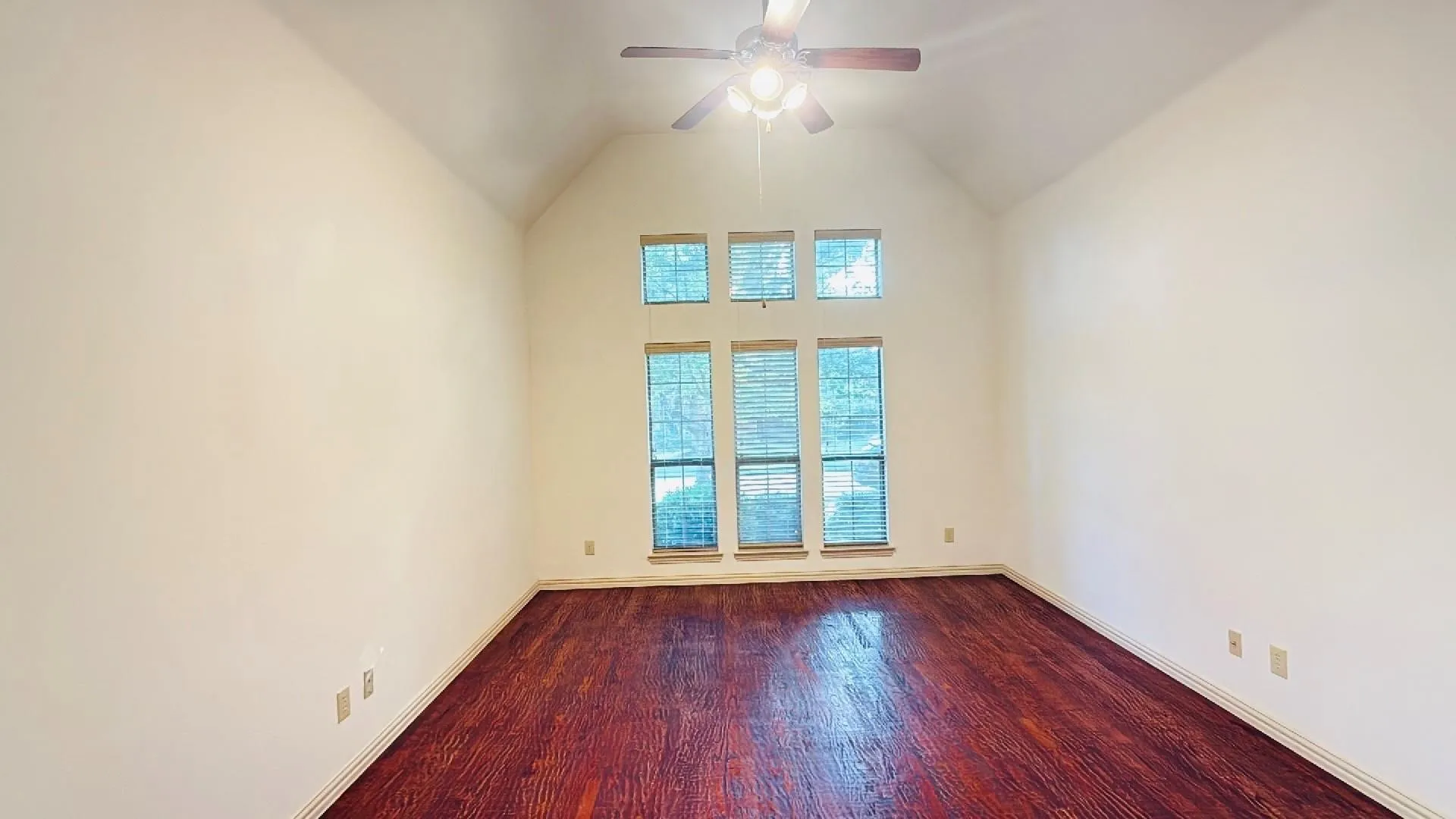 Vaulted ceiling with a ceiling fan, multiple windows with blinds, and wood-finish flooring