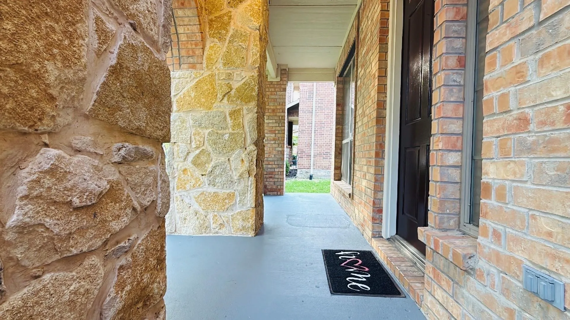 Brick exterior with stone accents, covered entry, dark-paneled front door, and a concrete porch