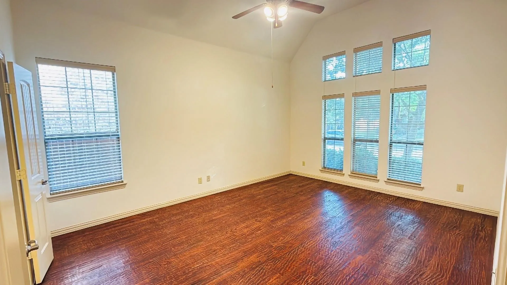 High vaulted ceiling with a ceiling fan, wood-finish flooring, and multiple windows with blinds