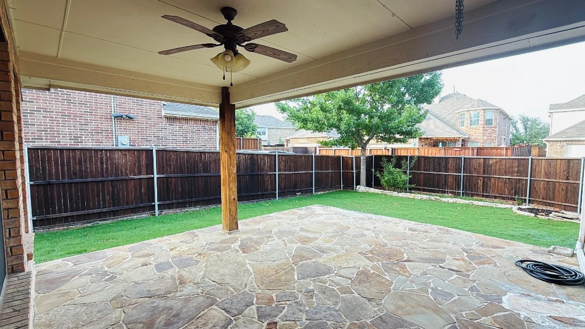 Covered patio featuring a ceiling fan, flagstone paving, and a wood support column