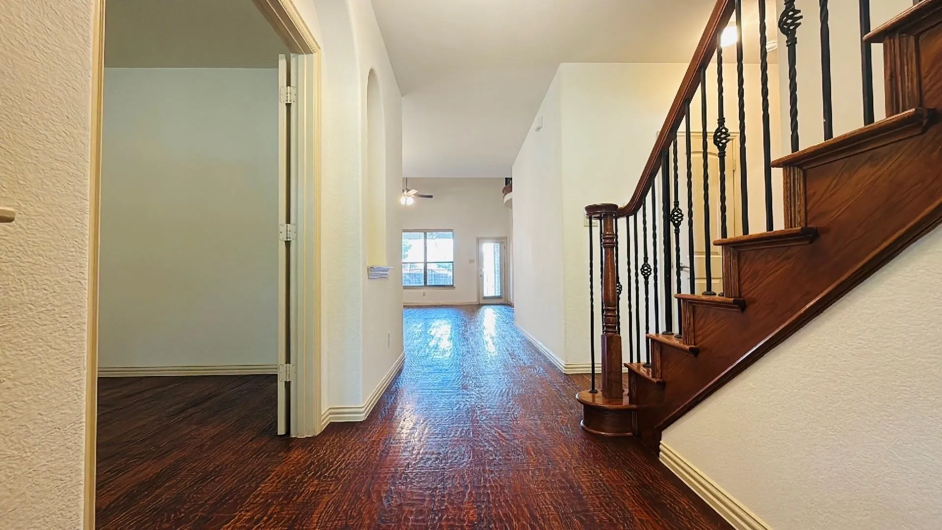 Rich wood-finish flooring throughout, prominent staircase with dark wood banister and wrought iron spindles, arched entryway, and tall ceilings