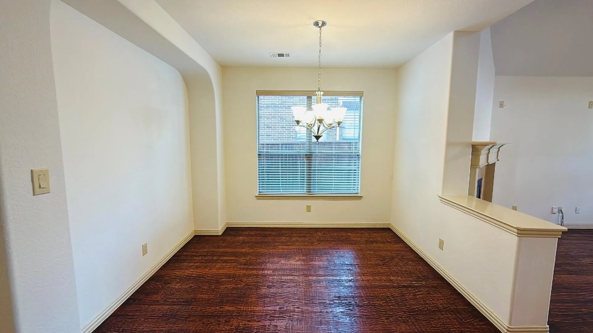 Hardwood-finish flooring, recessed architectural archway, window with blinds, and a chandelier lighting fixture