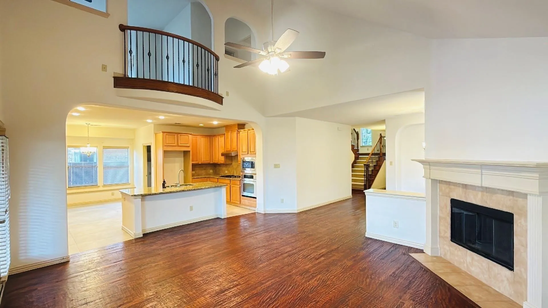 Vaulted ceilings, wood-finish flooring, a tile-surround fireplace, a kitchen with wood cabinetry, and a second-story interior balcony