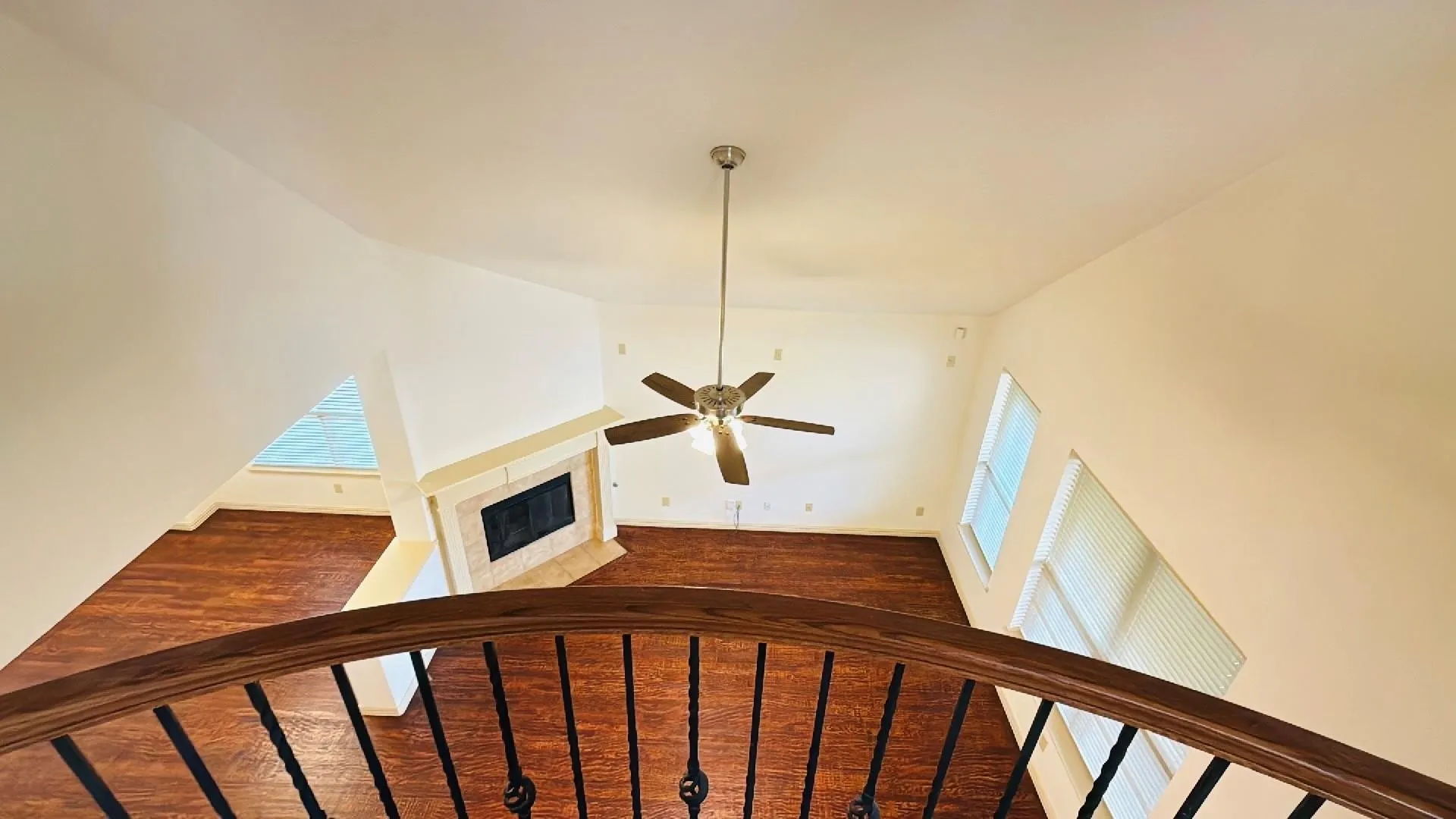 Vaulted ceiling with an attached fan, wood-finish flooring, and a fireplace with a stone surround