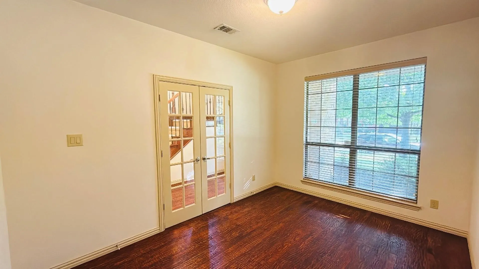 Rich wood-finish flooring, a large multi-pane window, and French doors with glass inserts