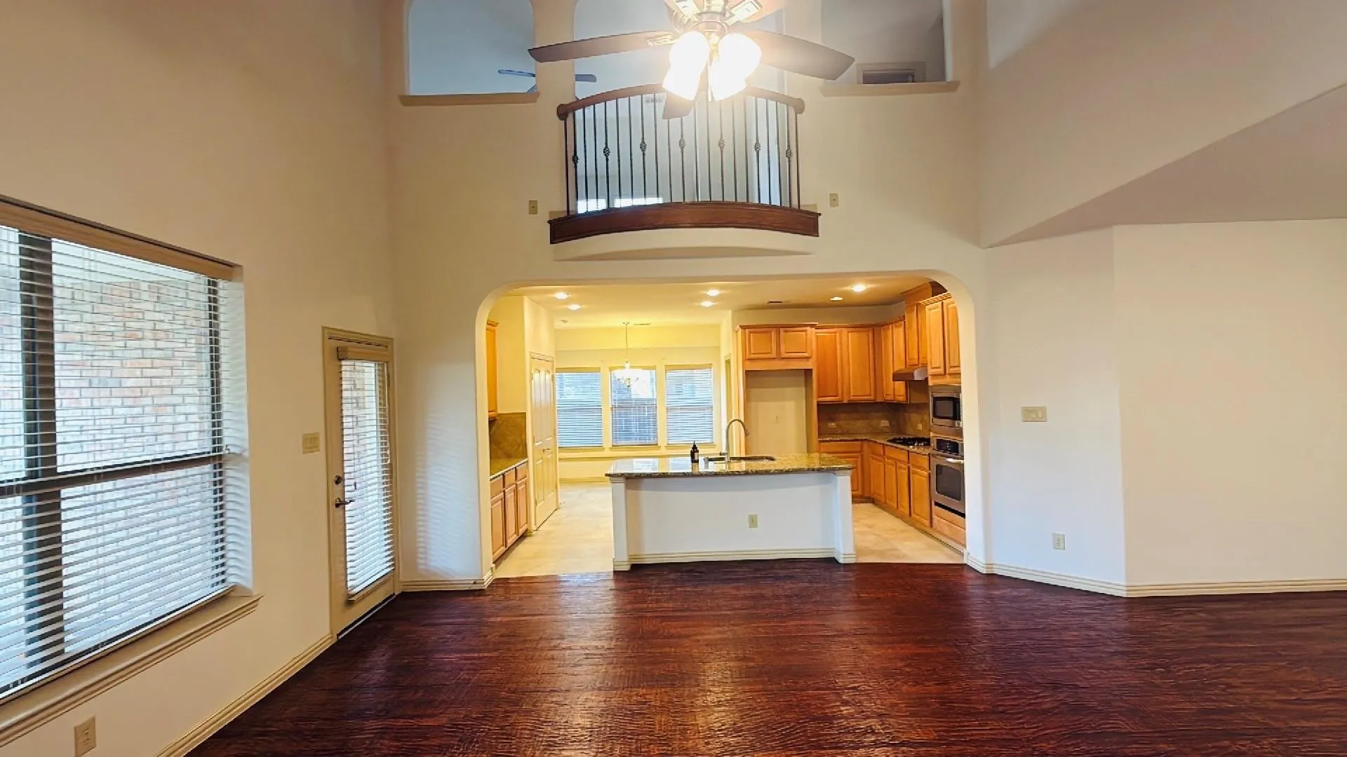Two-story living area with dark wood-finish flooring, featuring a ceiling fan, and arched entryways
