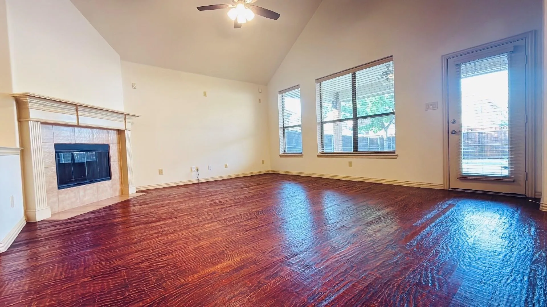 Vaulted ceiling, wood-finish flooring, fireplace with mantel, ceiling fan, and multiple windows