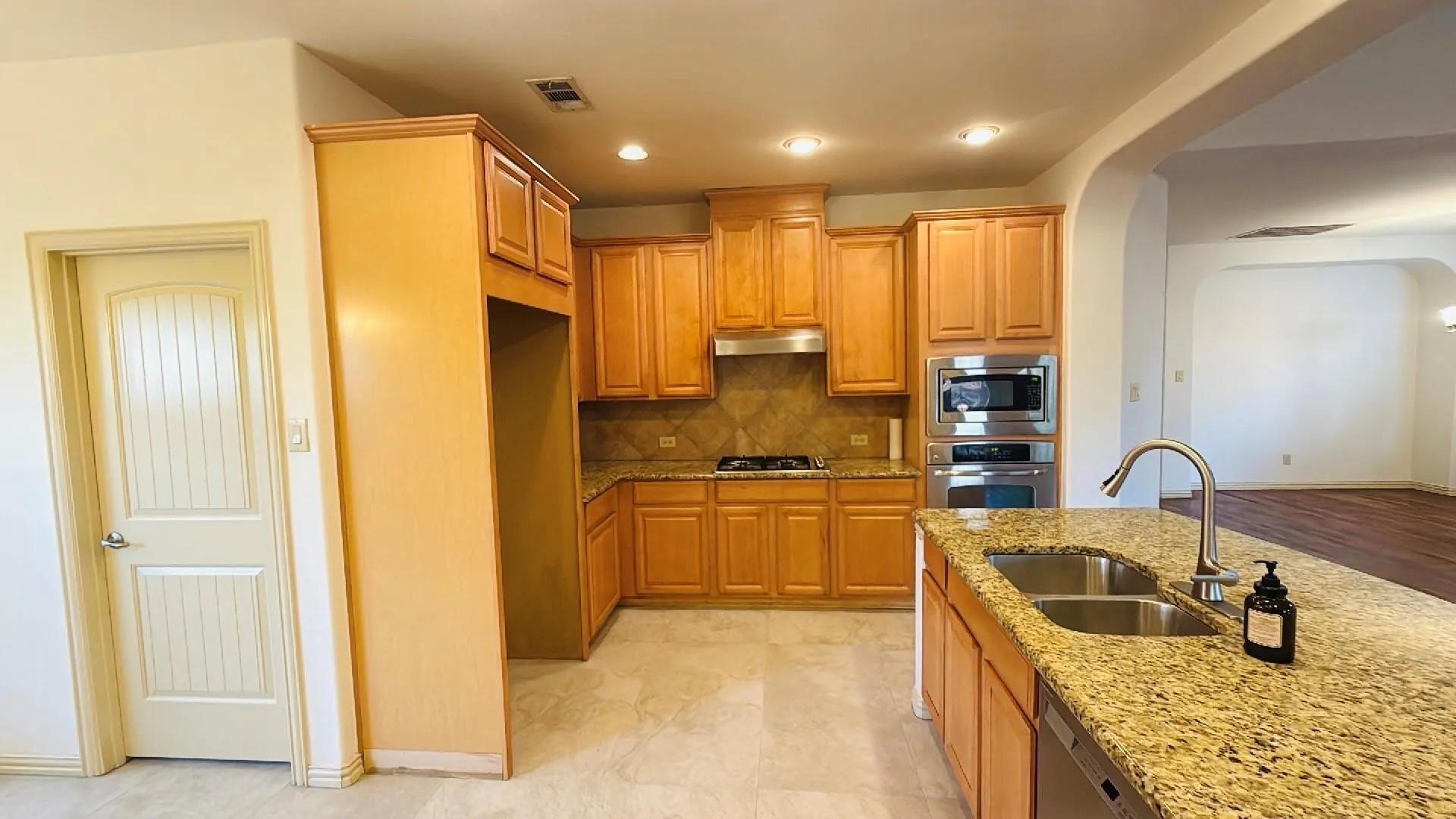 Kitchen featuring wood-finish cabinetry, granite countertops, tile flooring, and stainless steel appliances including a built-in oven and microwave