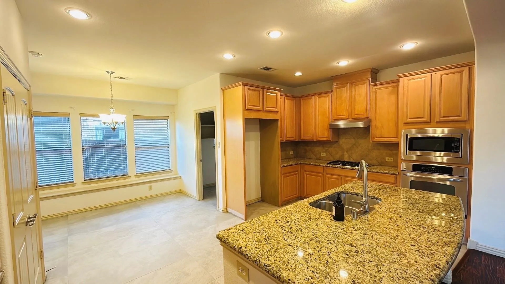 Kitchen featuring wood cabinetry, stainless steel appliances, a center island with a double basin sink, and granite countertops