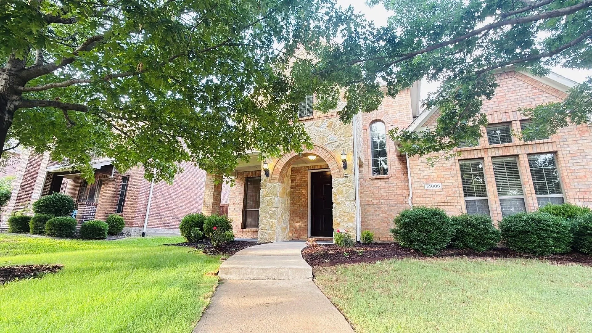 Brick and stone exterior featuring an arched entryway, established landscaping, and a concrete pathway