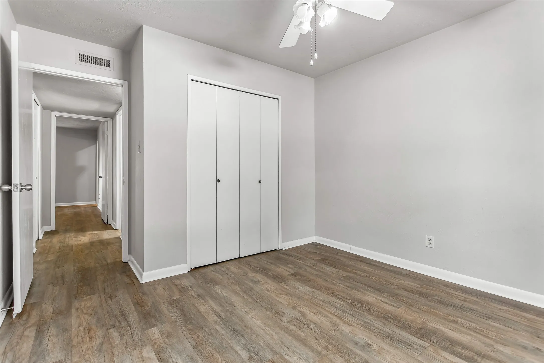 Wood-finish flooring, white bi-fold closet doors, ceiling fan with light fixture, and neutral painted walls