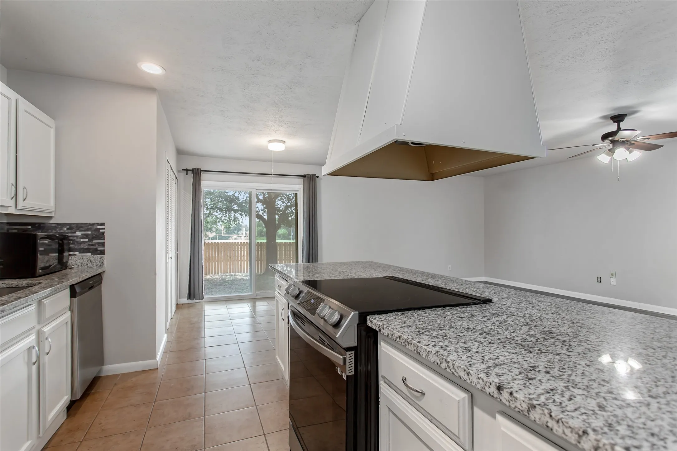 Tile flooring, white cabinetry, granite countertops, built-in electric range, and sliding glass door