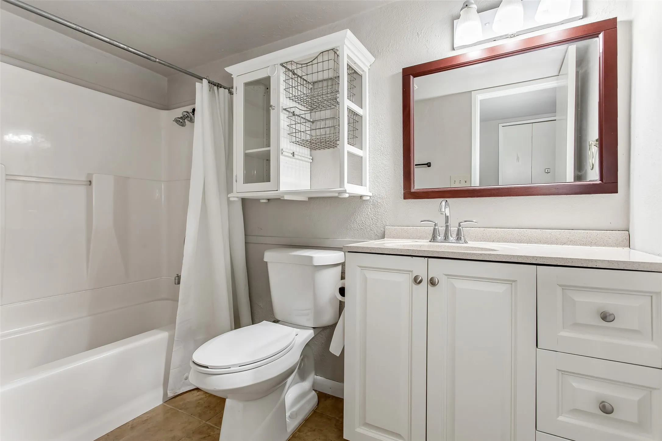 White vanity with a light-toned countertop, wood-framed mirror, and chrome fixtures