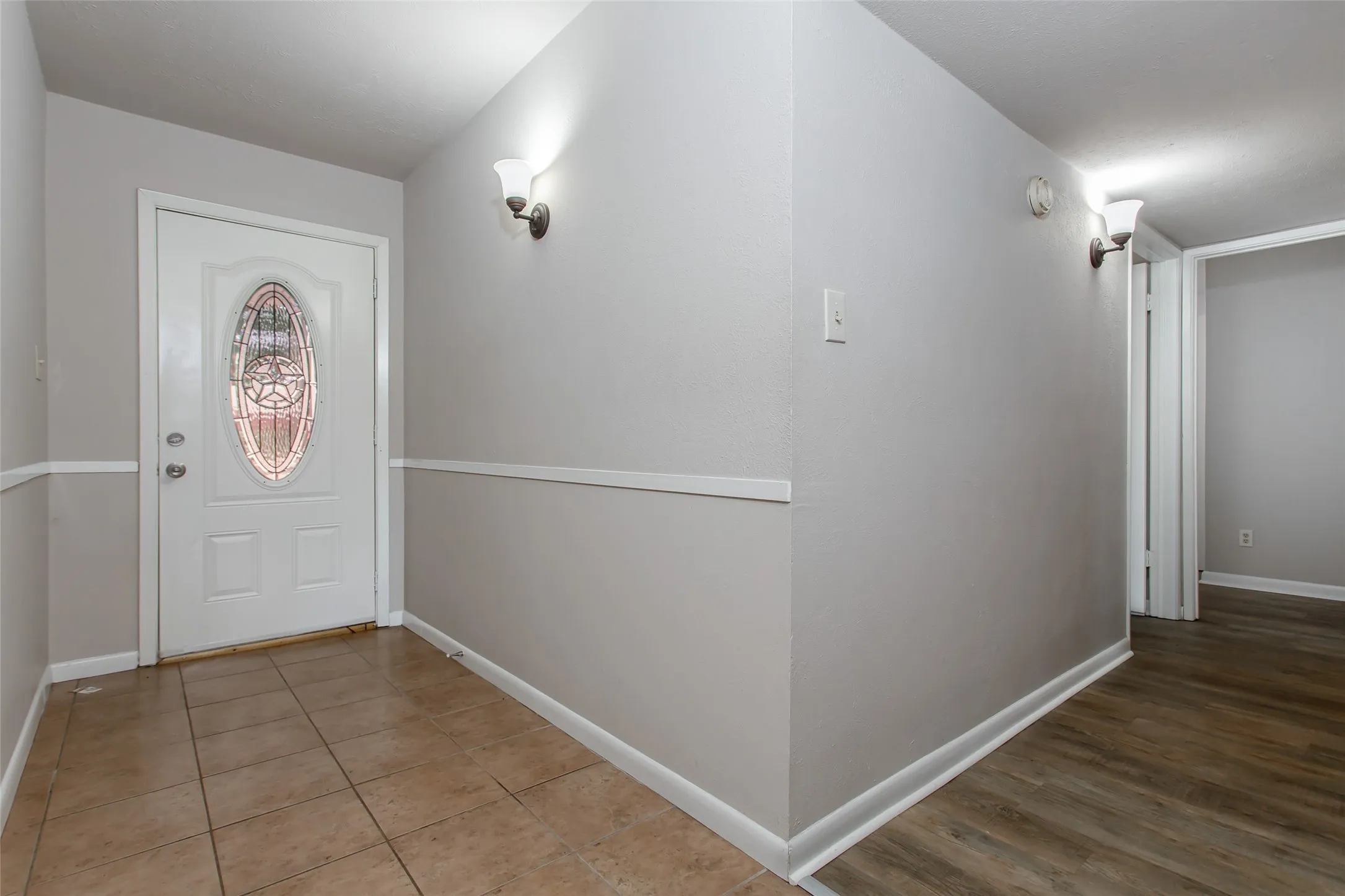 Entryway featuring a decorative glass panel door, ceramic tile flooring, and wall sconces