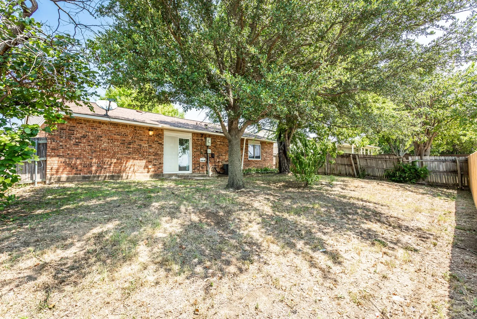 Brick exterior with a white rear door, mature trees, and wood fencing