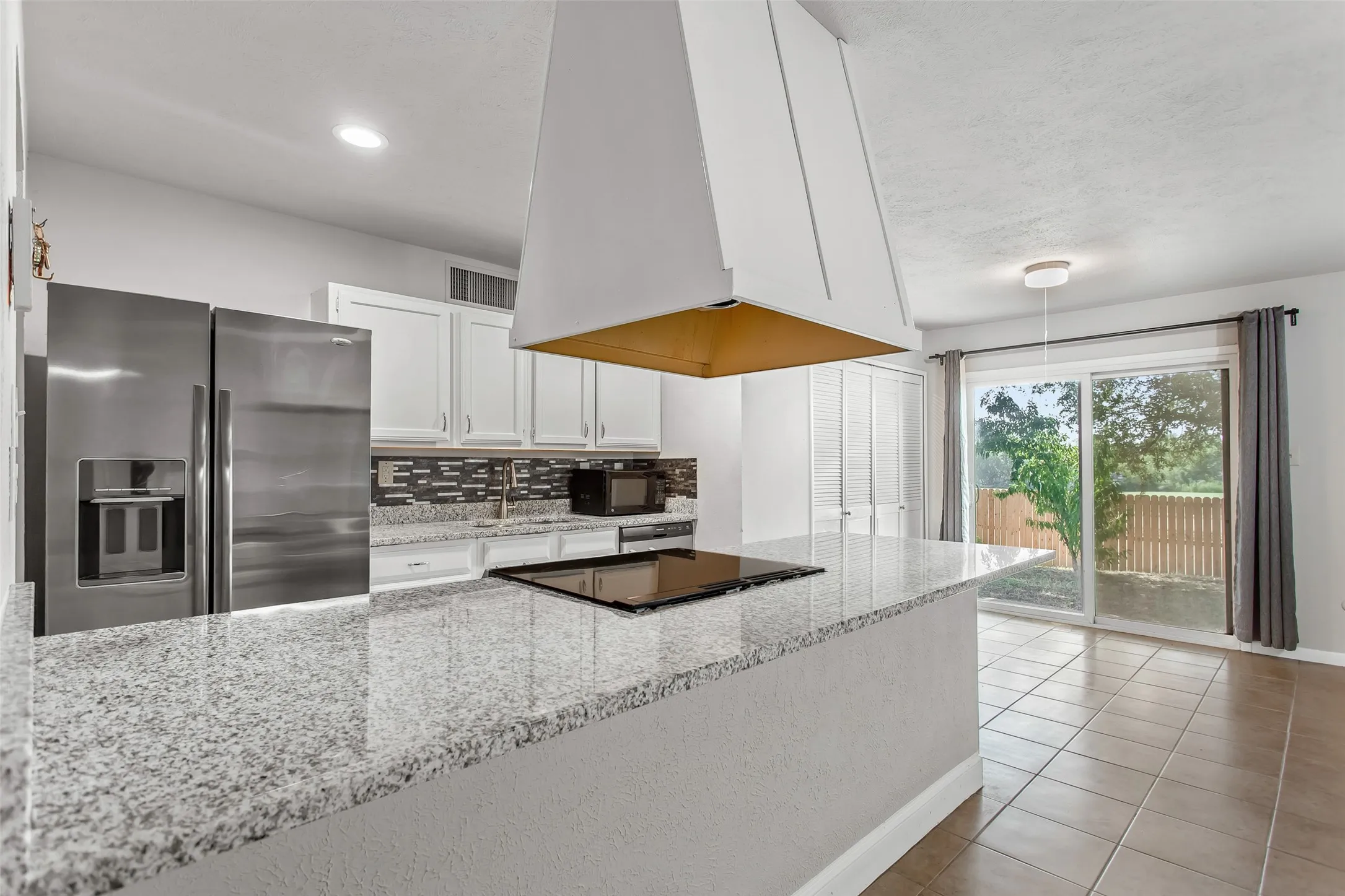 Kitchen featuring a large island with a cooktop, white cabinetry, stainless steel appliances, and a mosaic tile backsplash