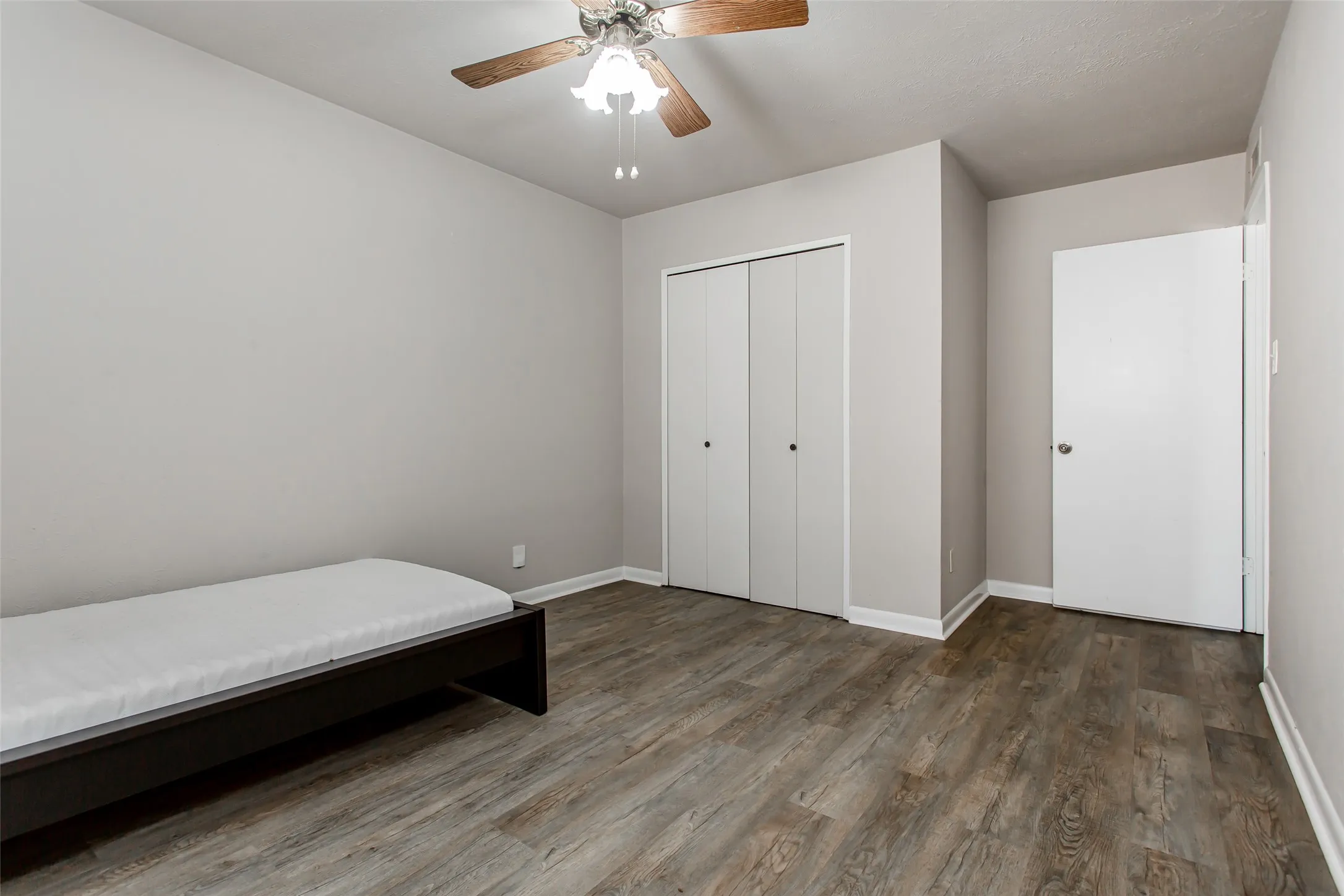 Wood-finish flooring, neutral wall tones, bi-fold closet doors, and an overhead ceiling fan