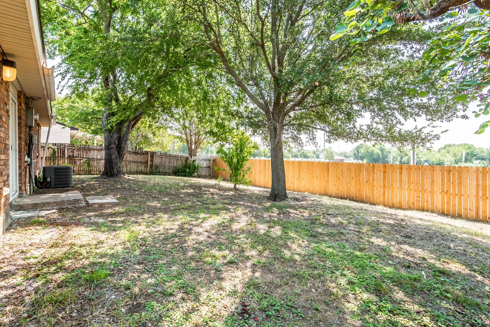 Expansive backyard featuring a new wood fence, mature shade trees, and a brick exterior